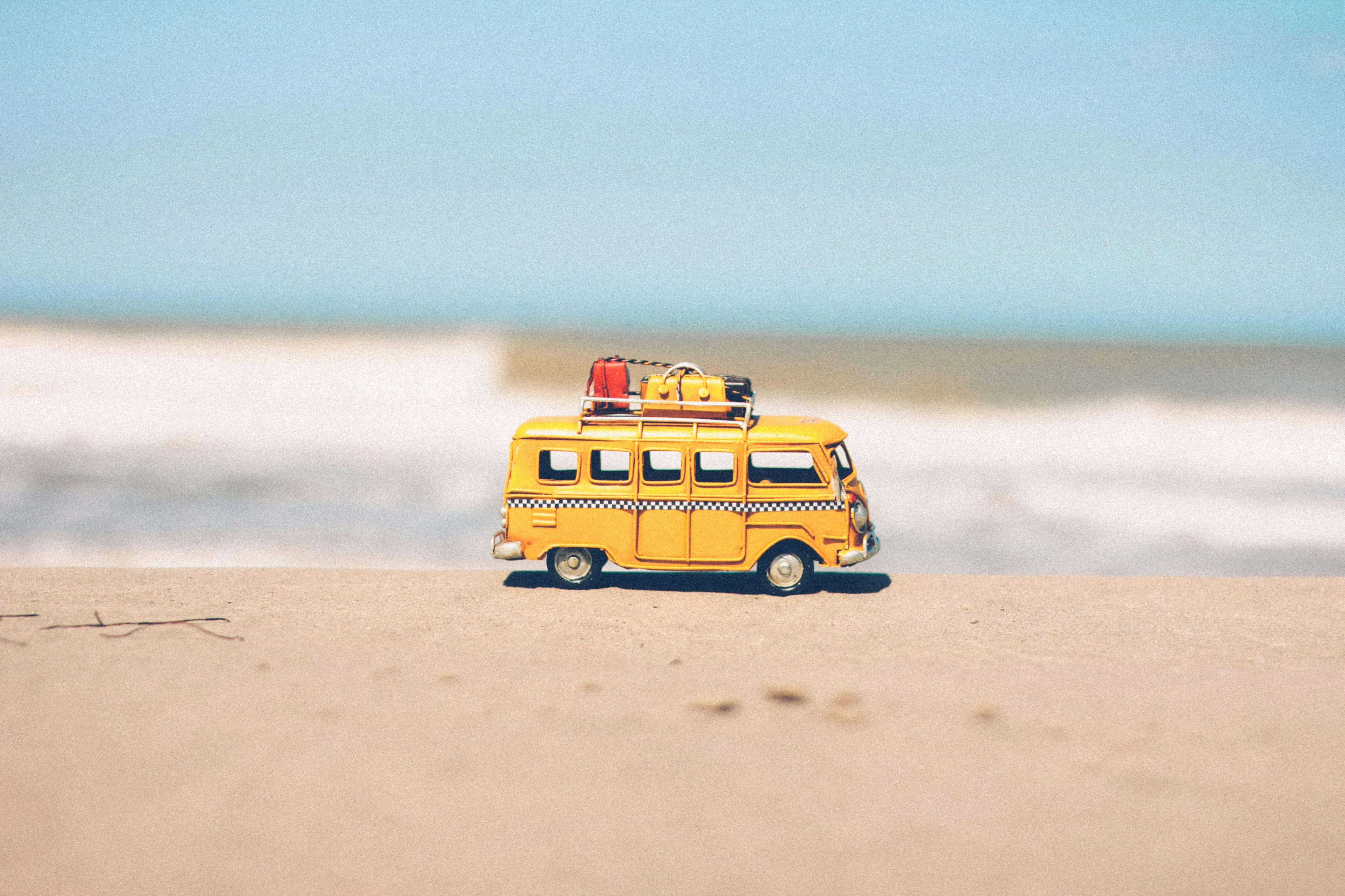 Yellow Bus Toy on Beach Sand with Blue Ocean Background
