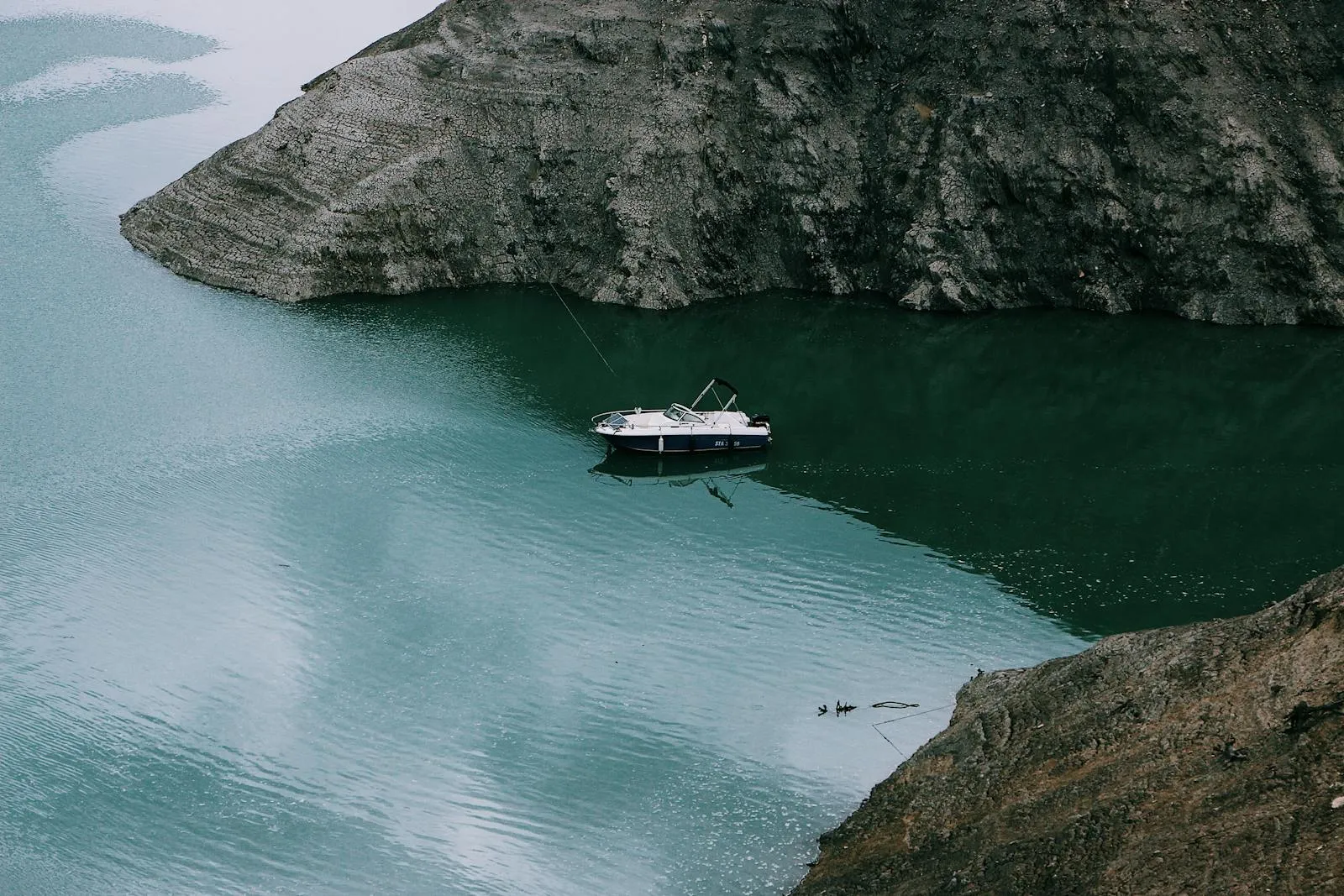 A Small Boat Anchored Near Rocky Cliffs and Calm Green Water