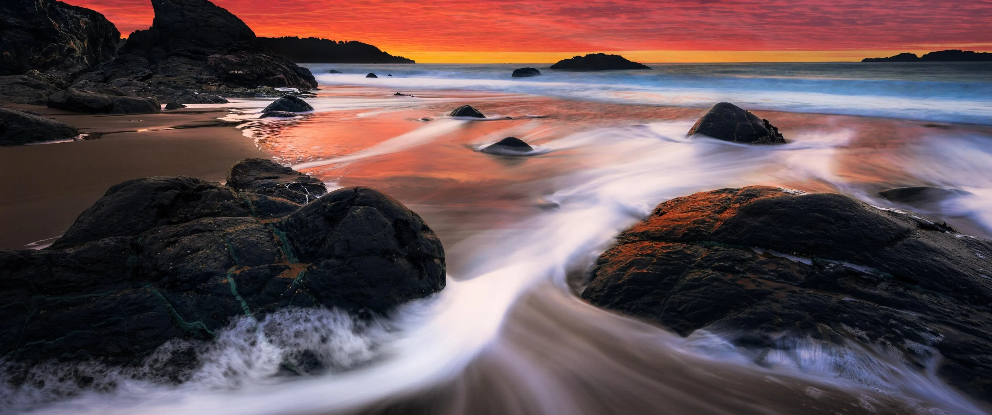 Black Rocks with a Colorful Glowing Beach Sunset Wallpaper