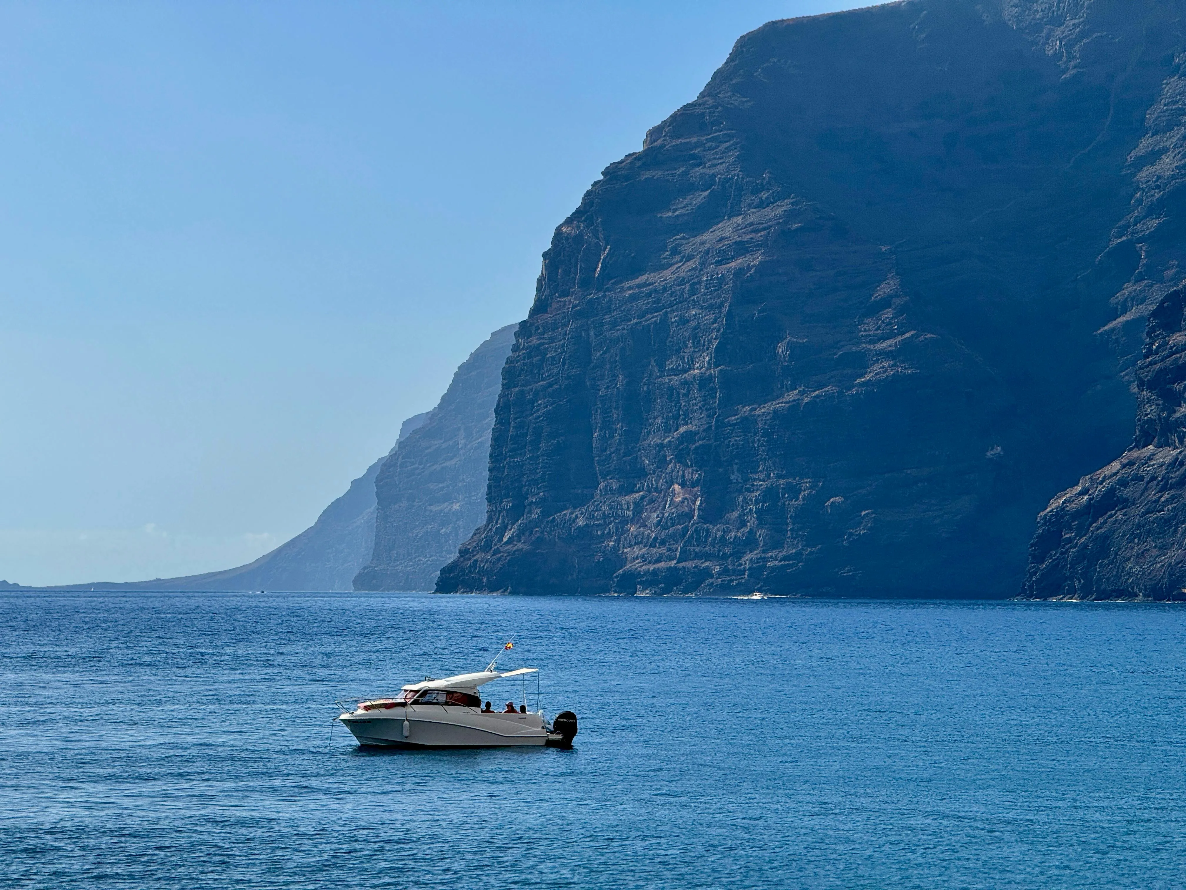 Boat Floats Calmly Near Towering Seaside Mountain Wallpaper