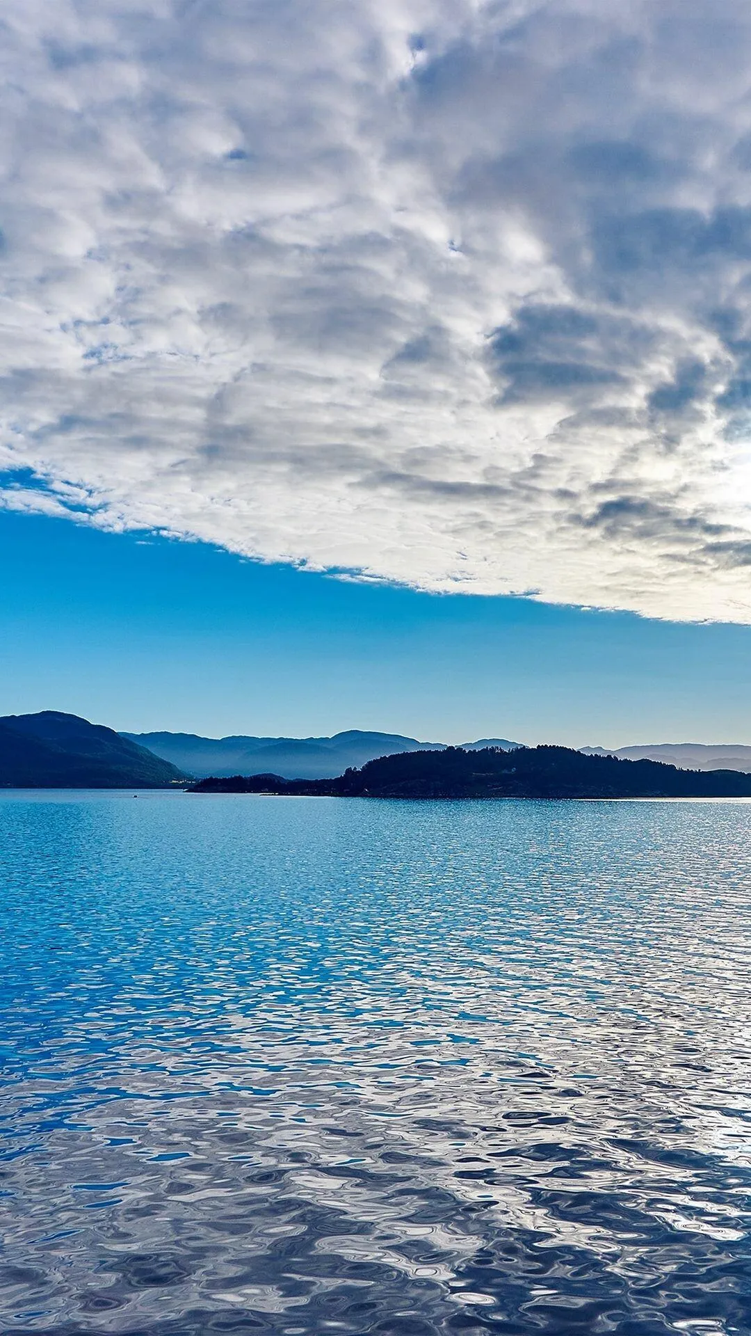 Calm Ocean with Small Islands Under a Cloudy Blue Sky