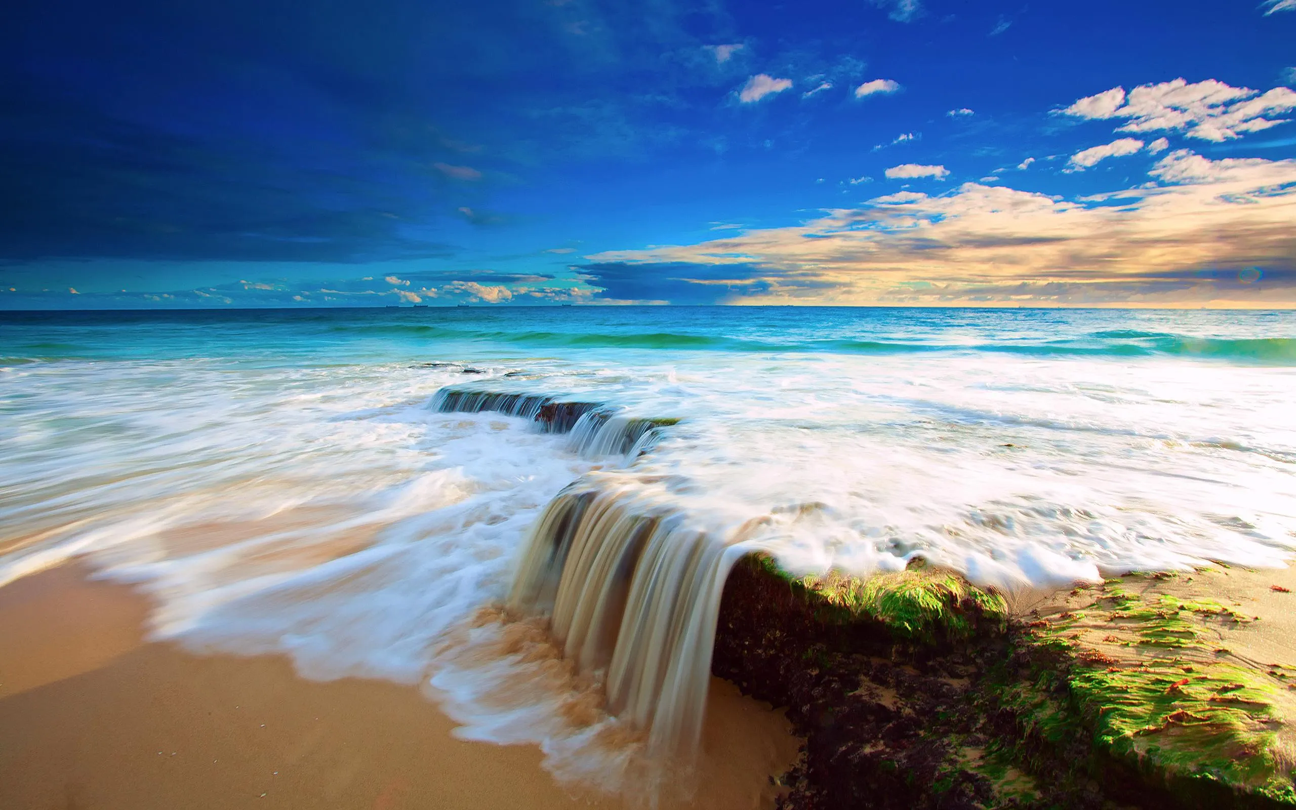 Crashing Wave on Sandy Beach with Bright Blue Sky Wallpaper