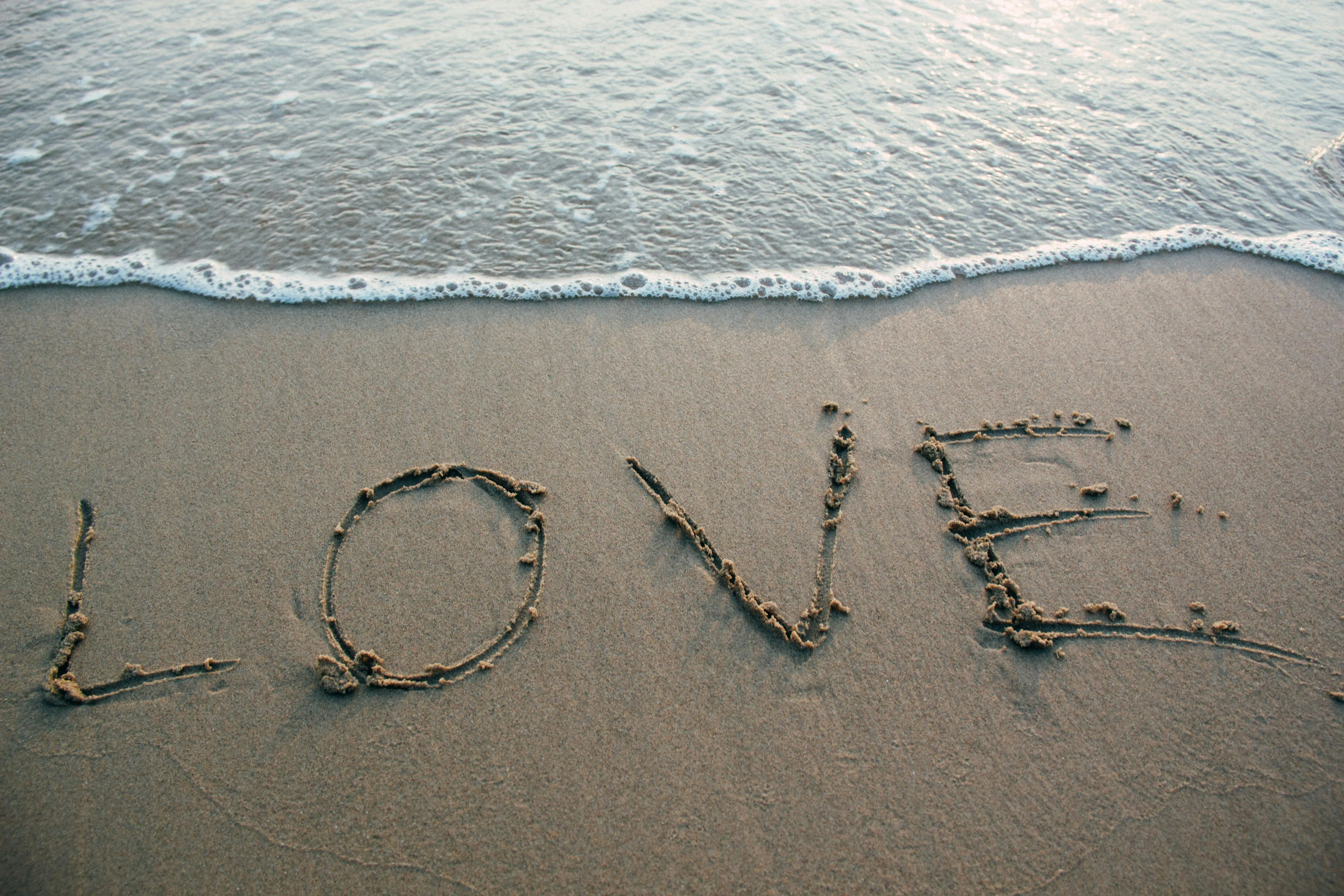 Love Written in Sand with a Gentle Ocean Wave Free Wallpaper