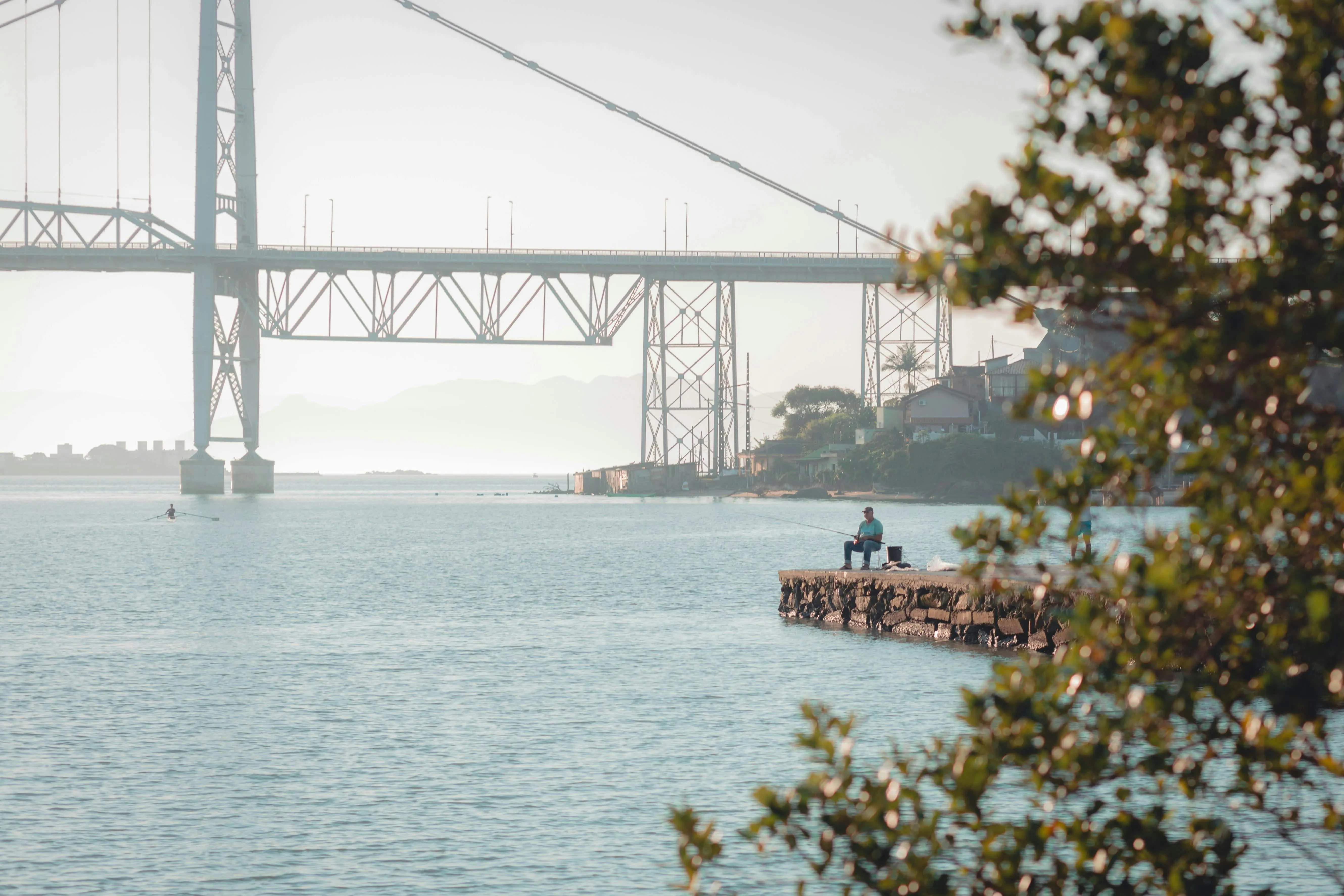 Man Fishing in a Lake Under a Large Metal Suspension Bridge