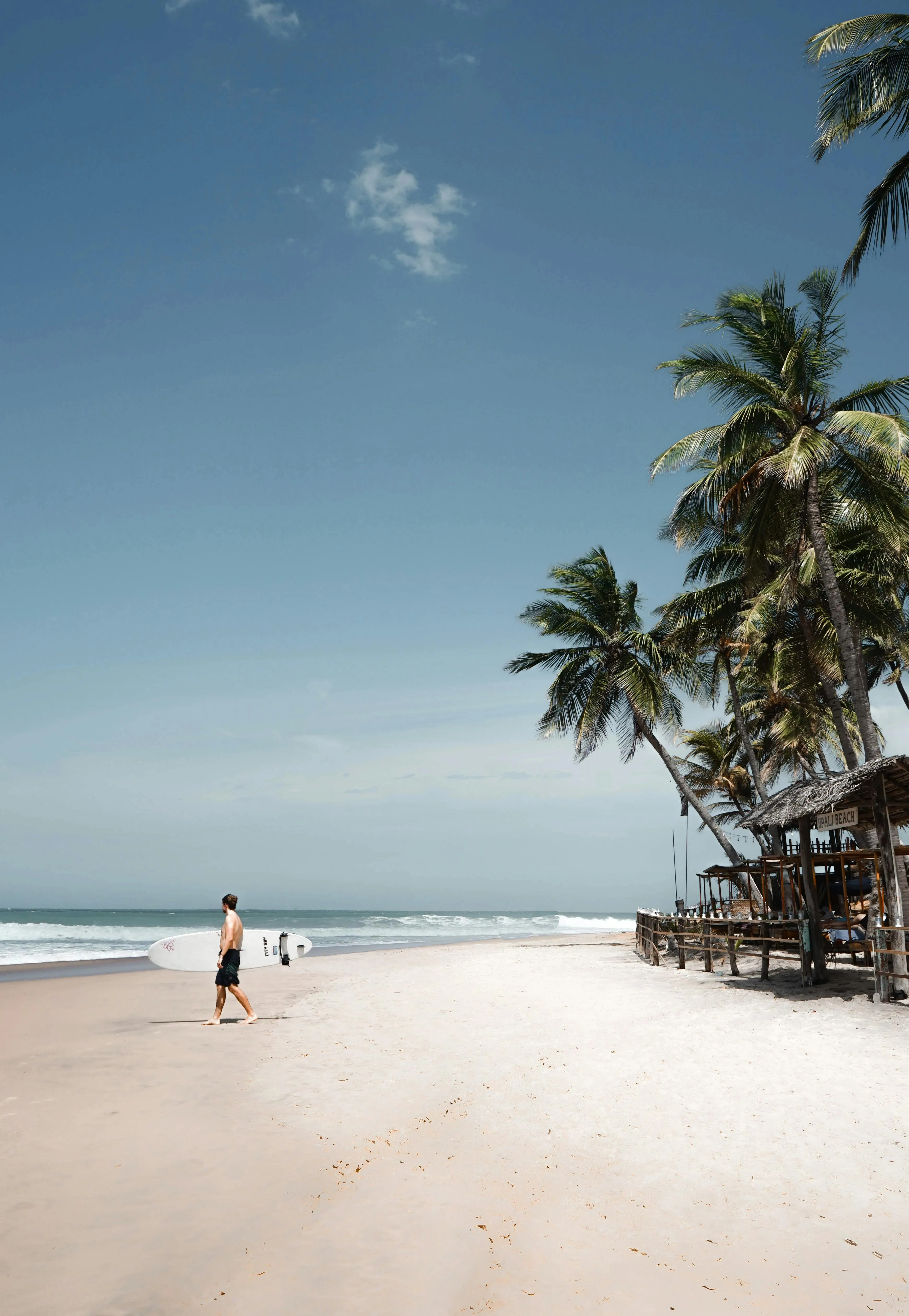 Man Walking on an Empty White Beach Under a Blue Sky