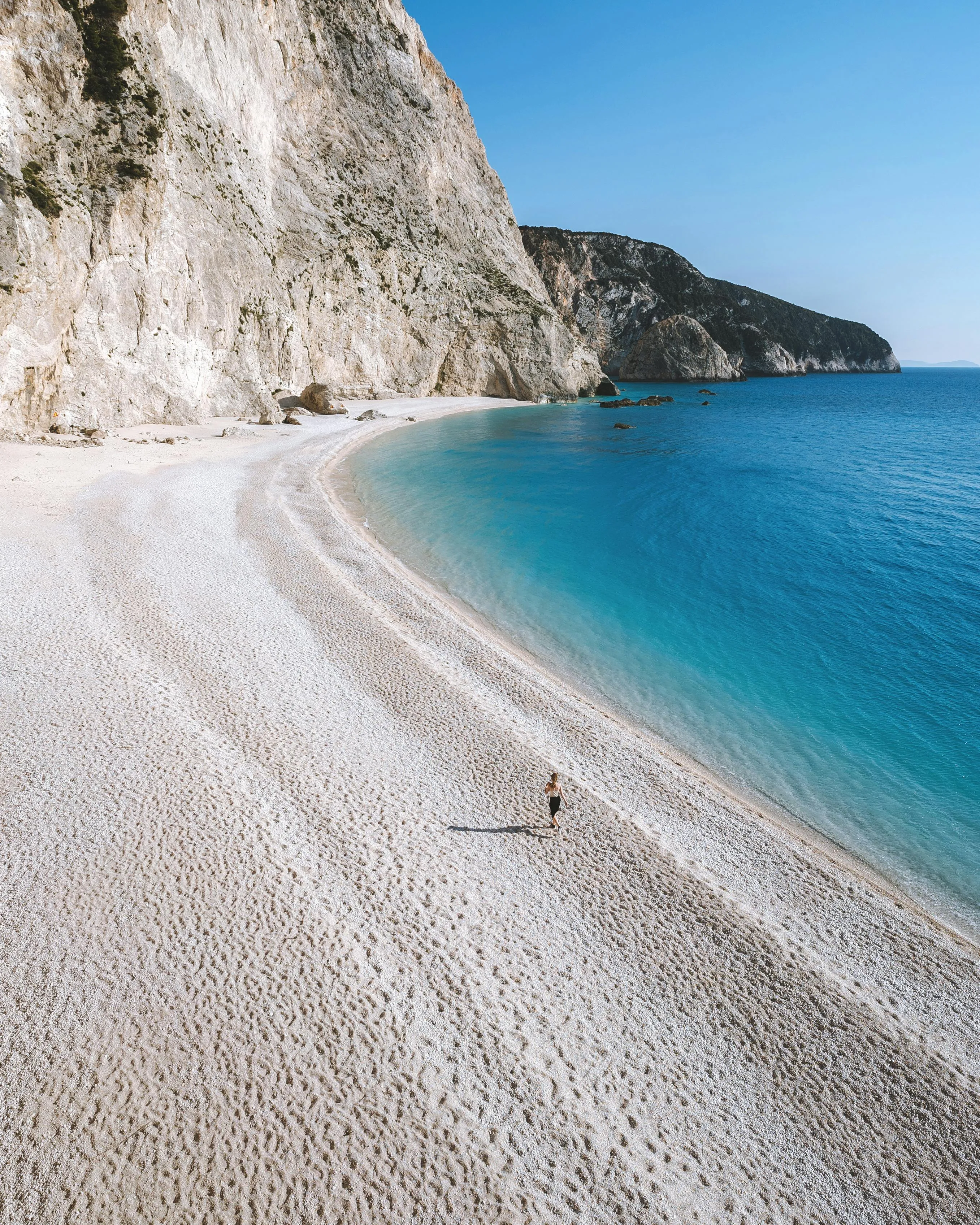 Man Walking on a Beach with White Sand and Rocky Cliffs