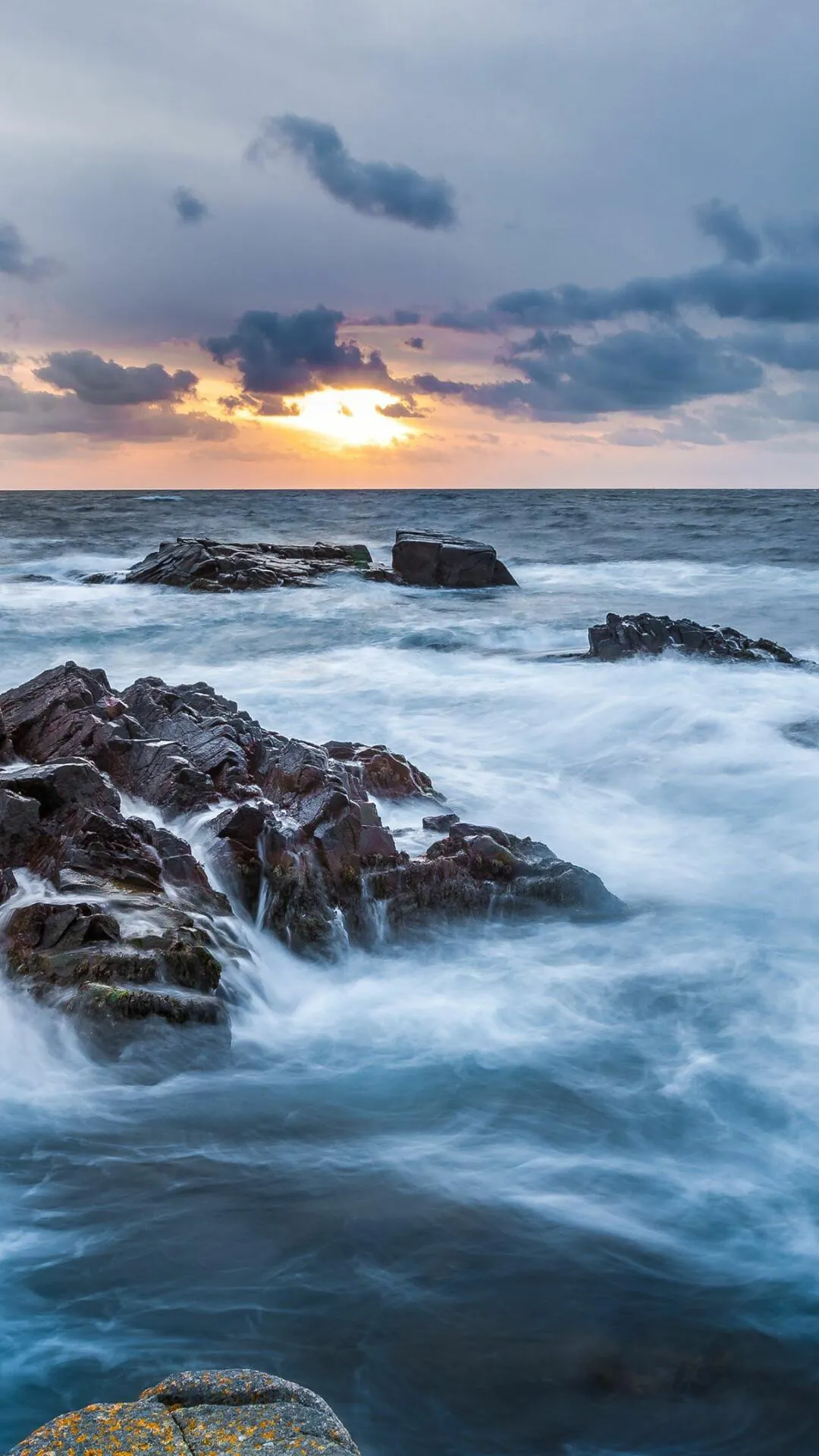 Ocean Waves Crash on Rocks During a Vibrant Evening Sky
