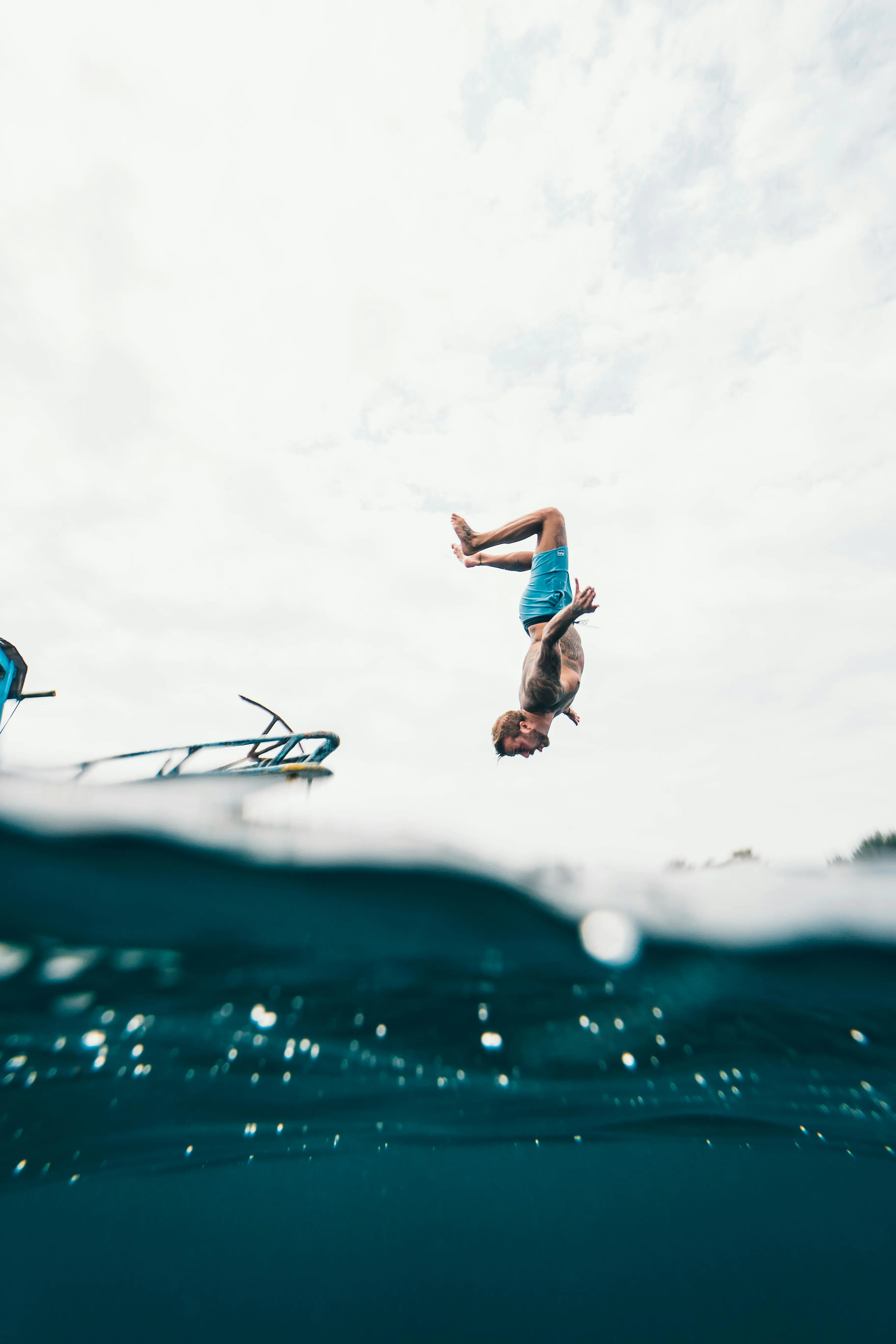 Person Mid Air Jumping into Water Against a Bright Sky