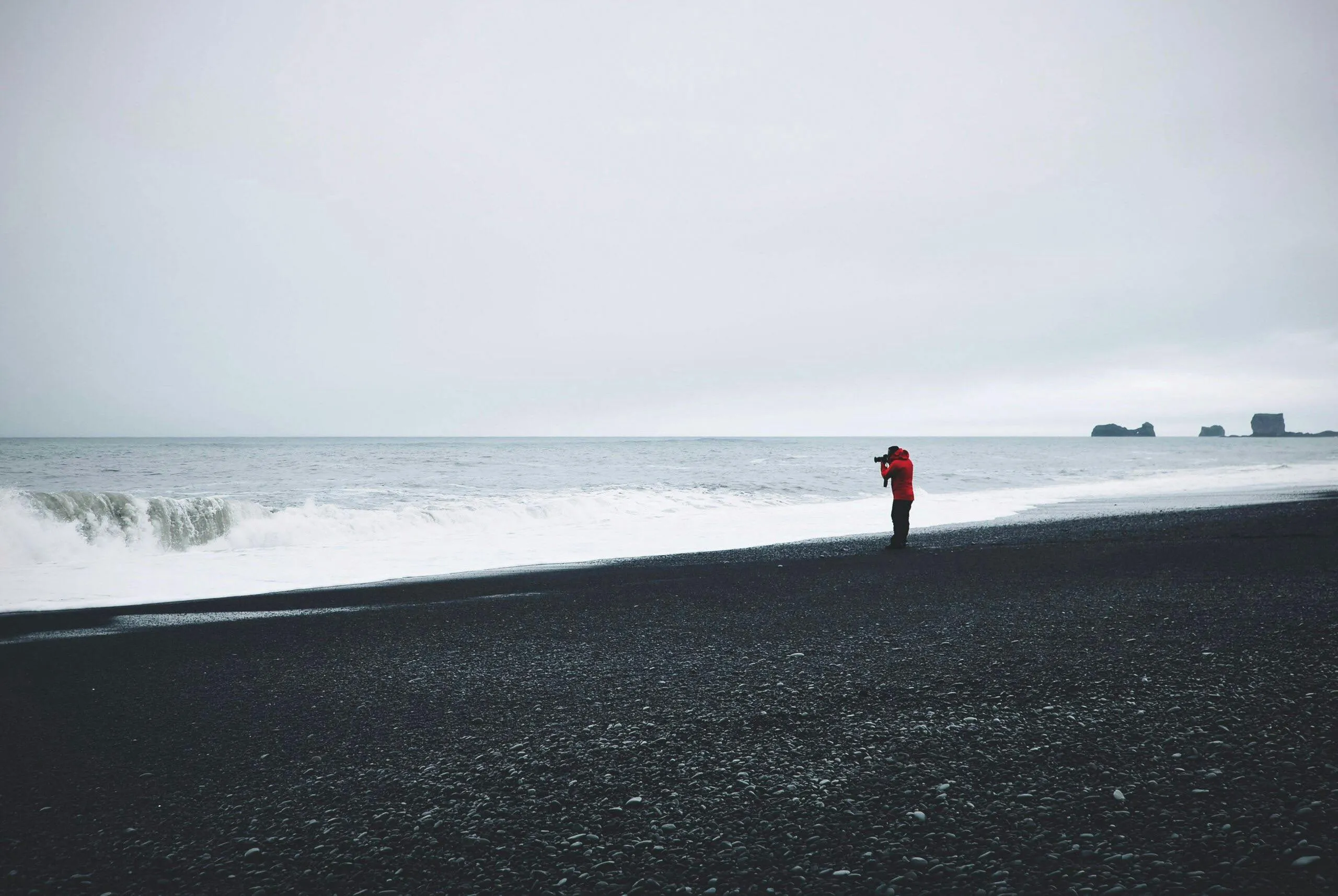 Person Standing Alone on a Black Sand Beach in Foggy Weather