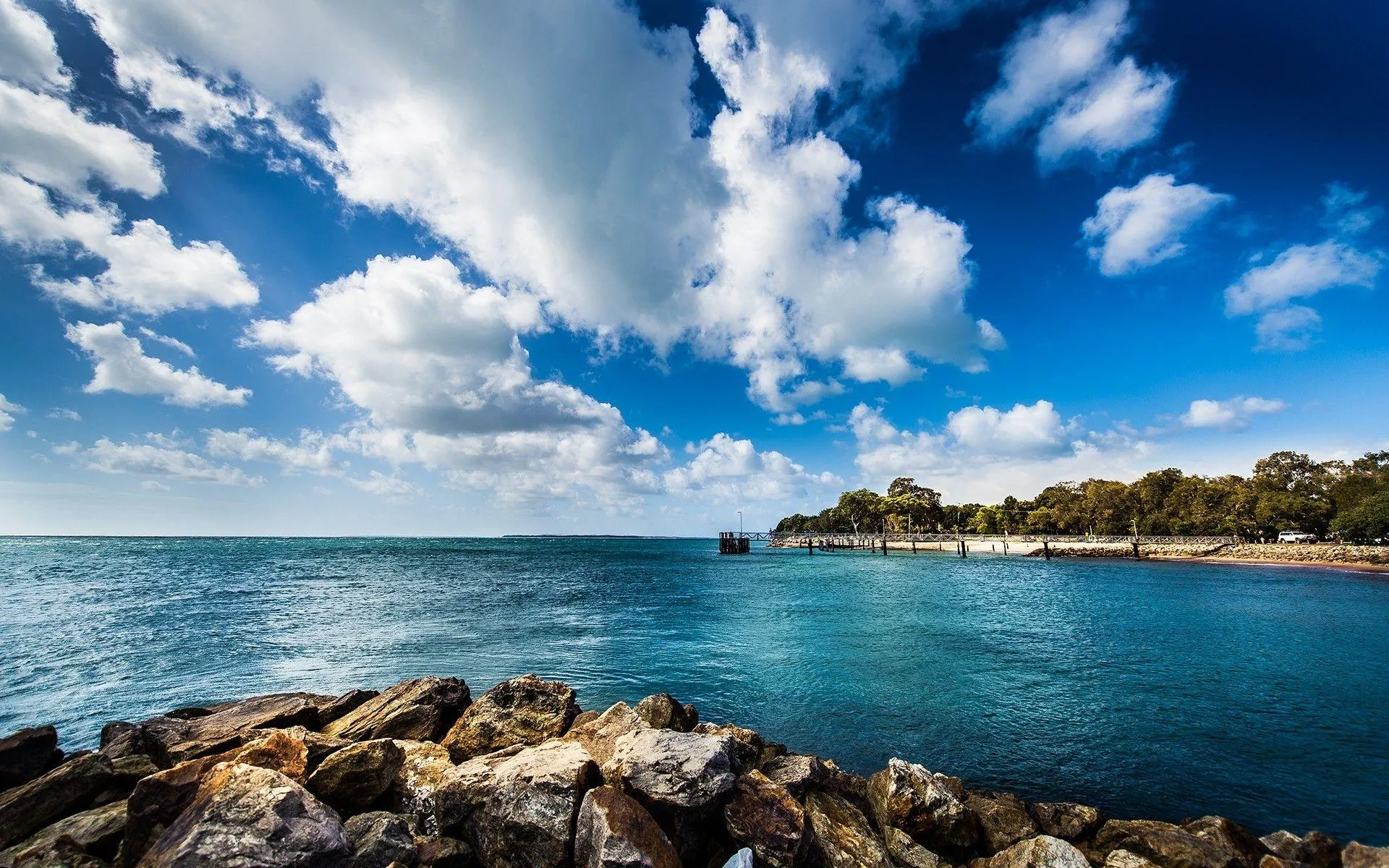 Rocky Coastline Under Bright Sky with Scattered White Clouds