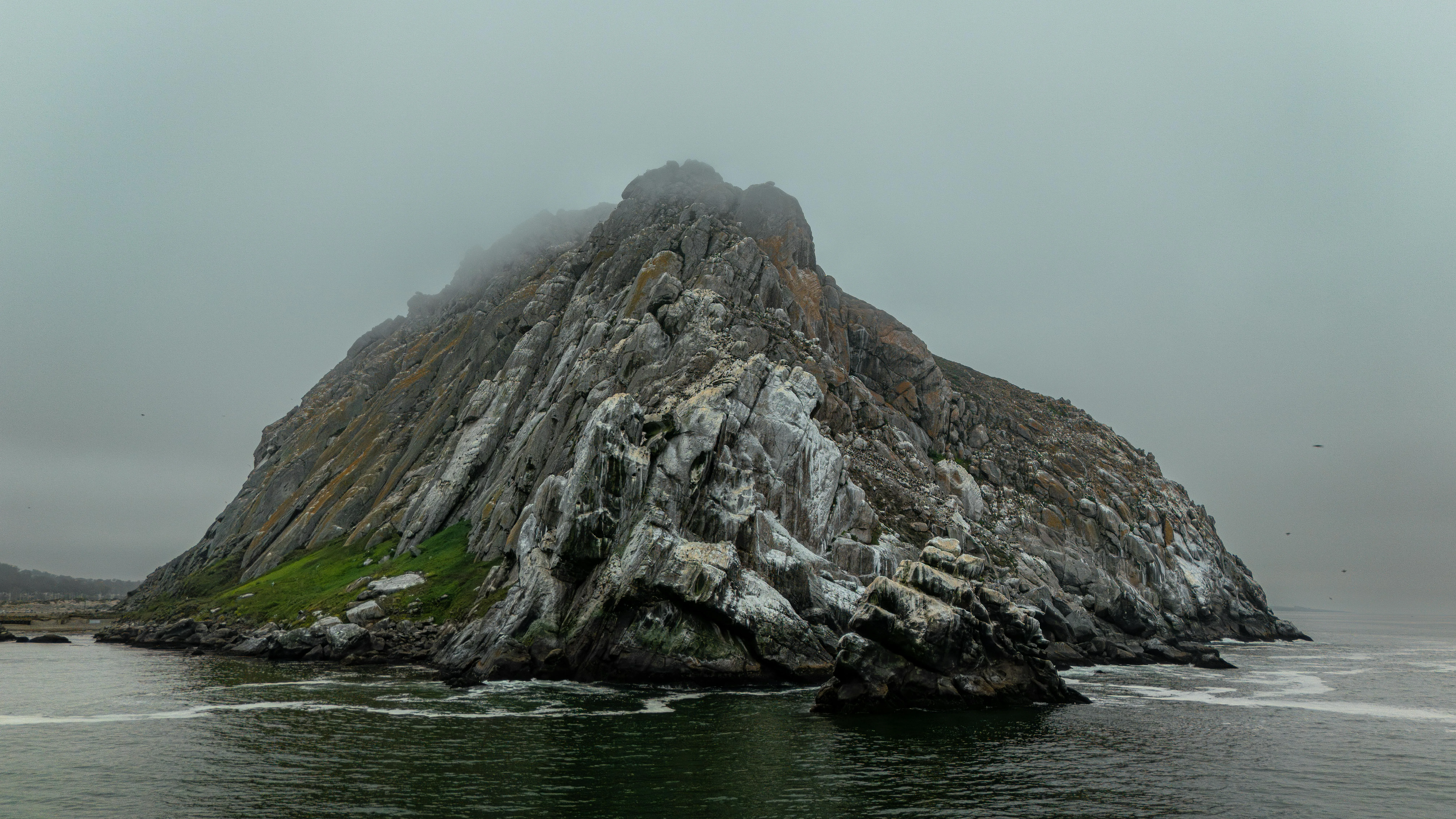 Rocky Island Stands Alone in Calm Gray Ocean Water Wallpaper