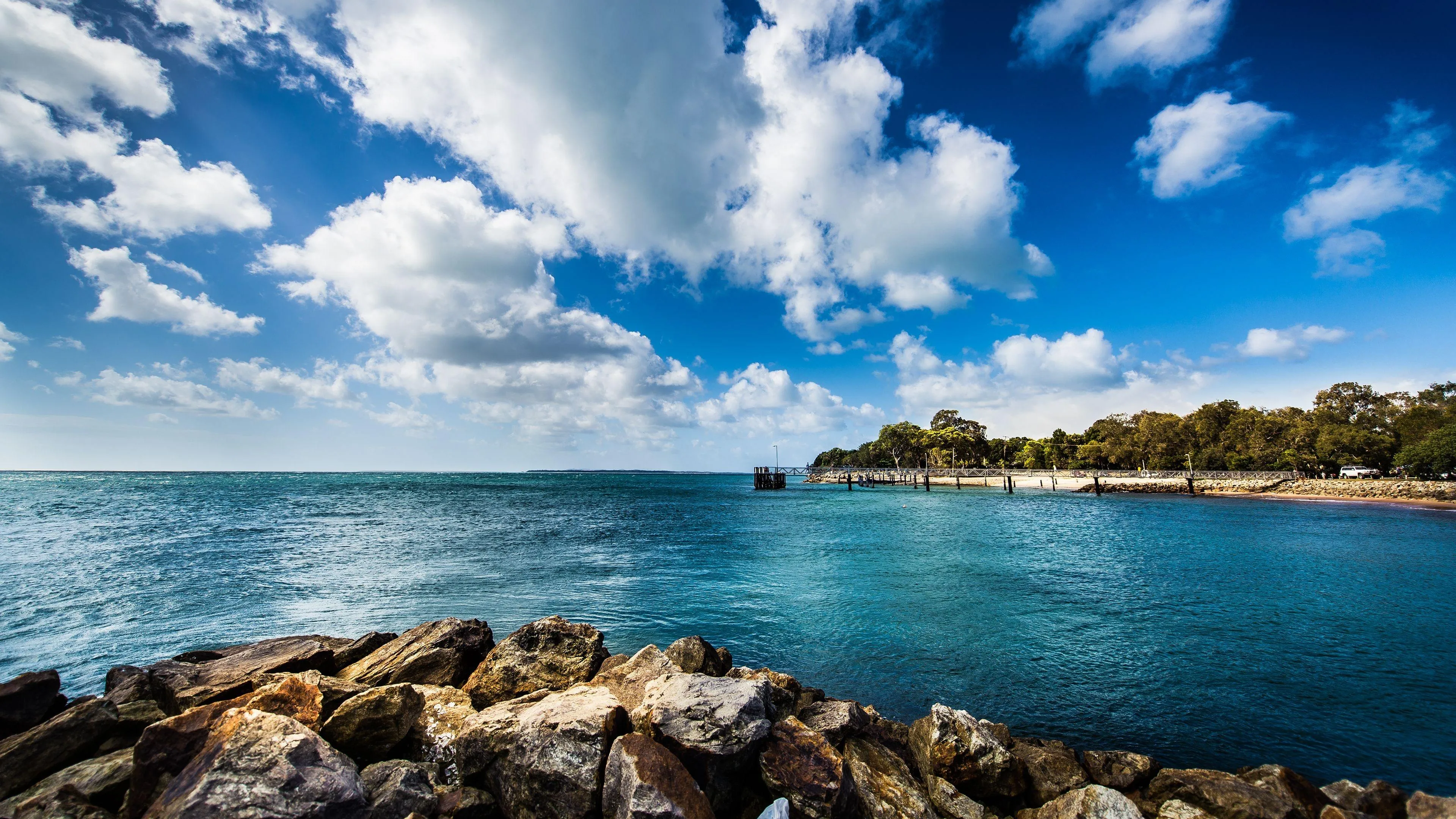 Rocky Shoreline Under Blue Sky with Fluffy White Clouds