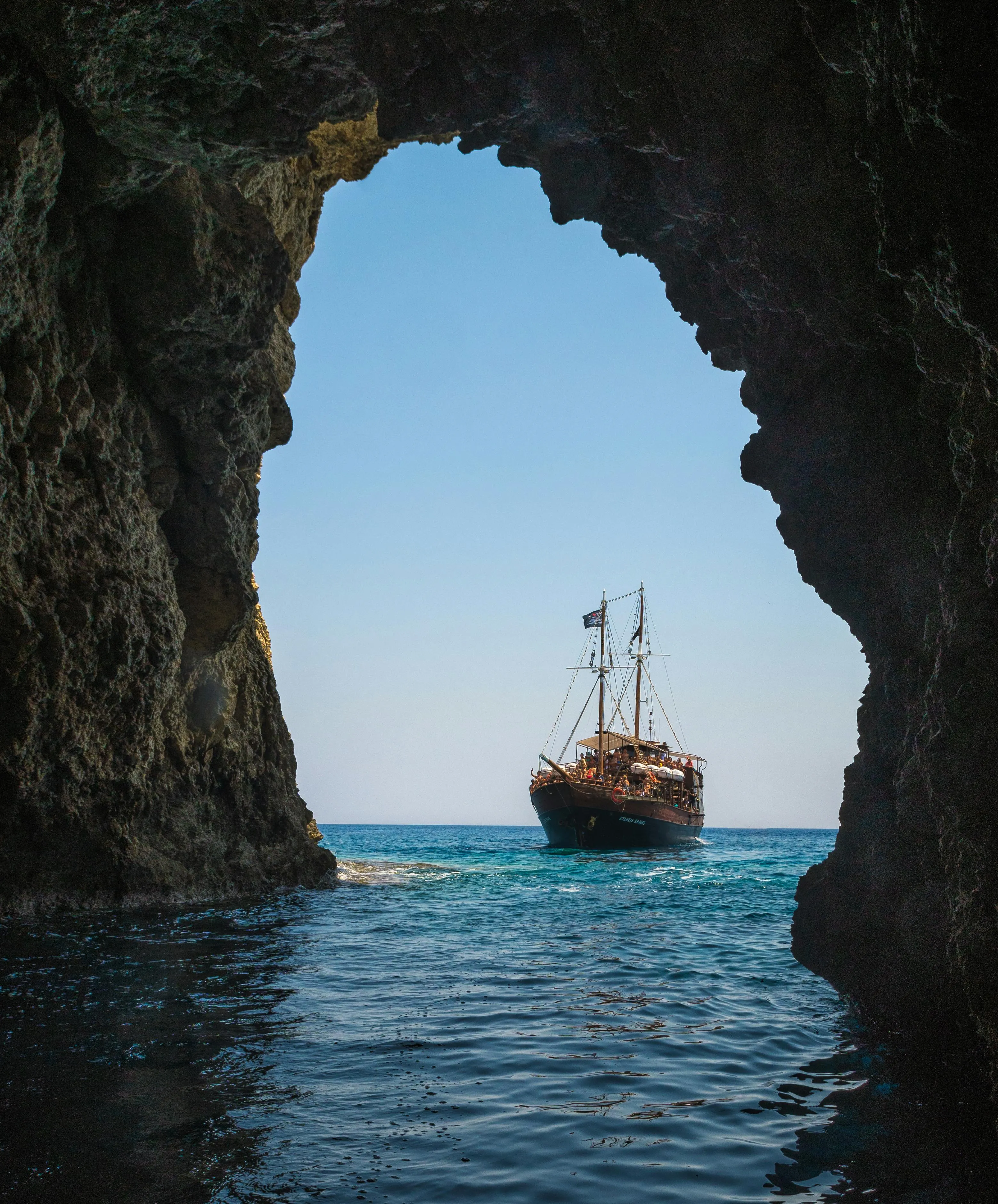 Sailing Ship Framed by Rocky Cliffs and Open Blue Sea