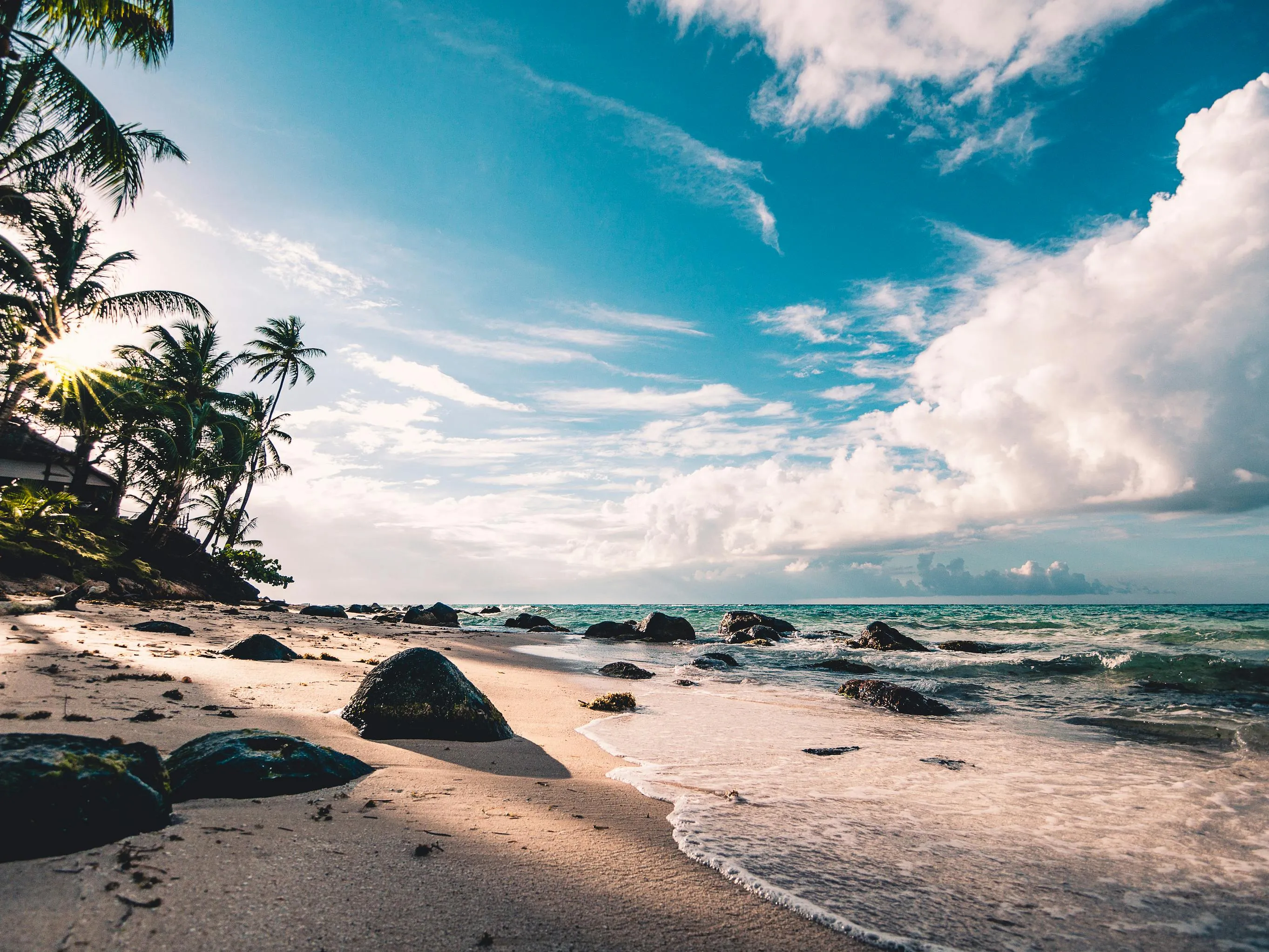 Serene Rocky Beach Under a Bright Cloudy Sky Free Wallpaper