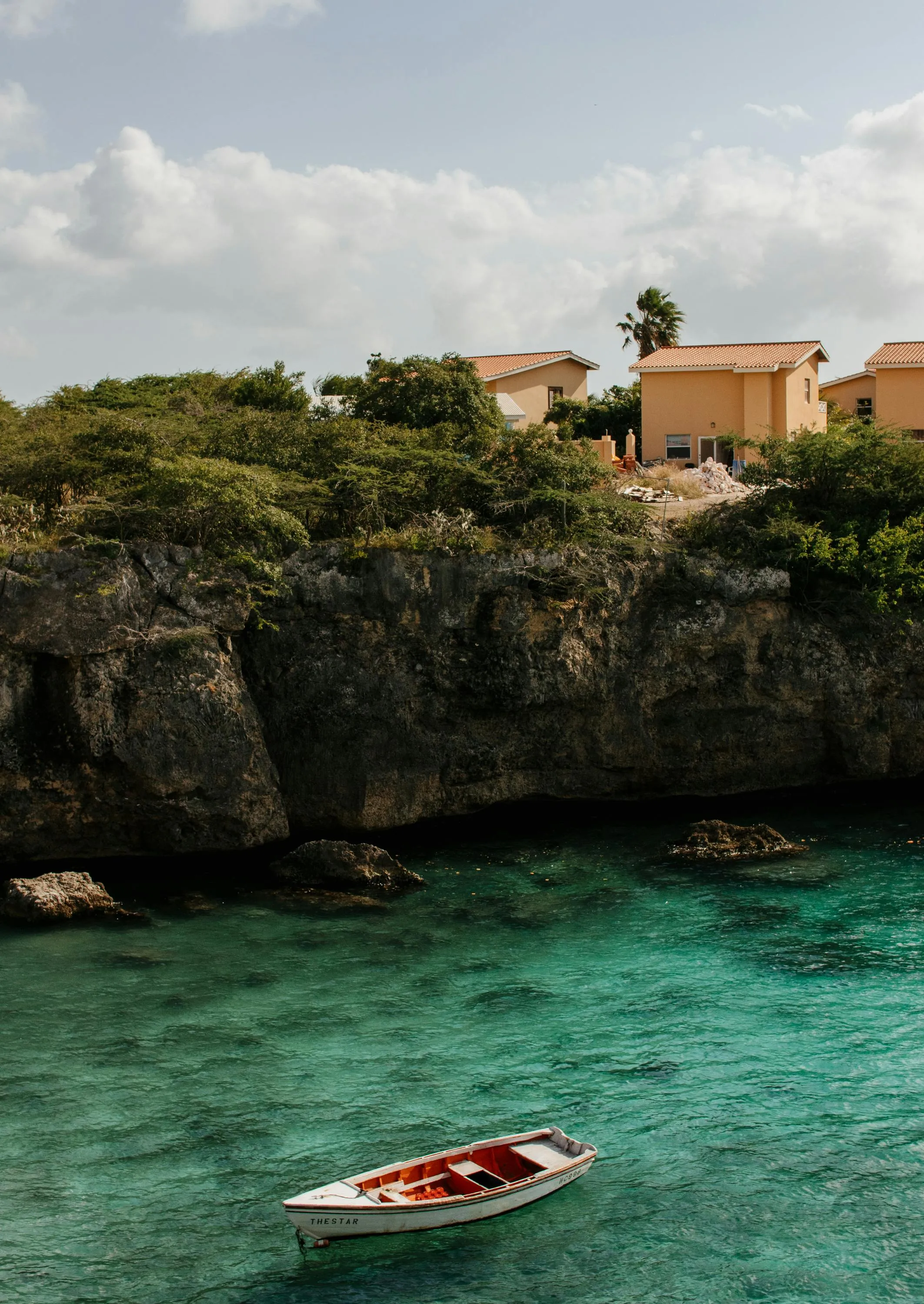 Single Red Boat Floating Near a Rocky Beach and Houses