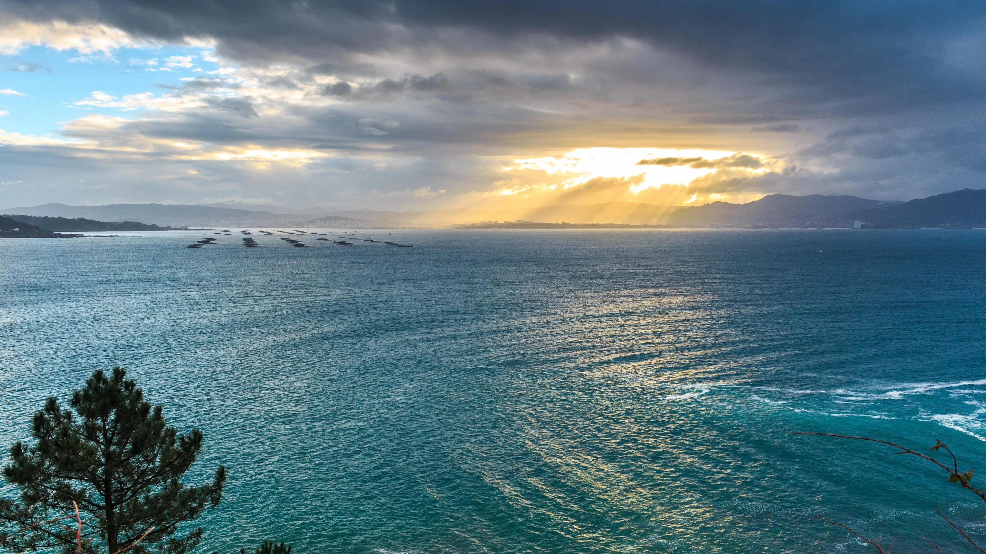 Sun Breaking Through Clouds over Calm Ocean and Shoreline