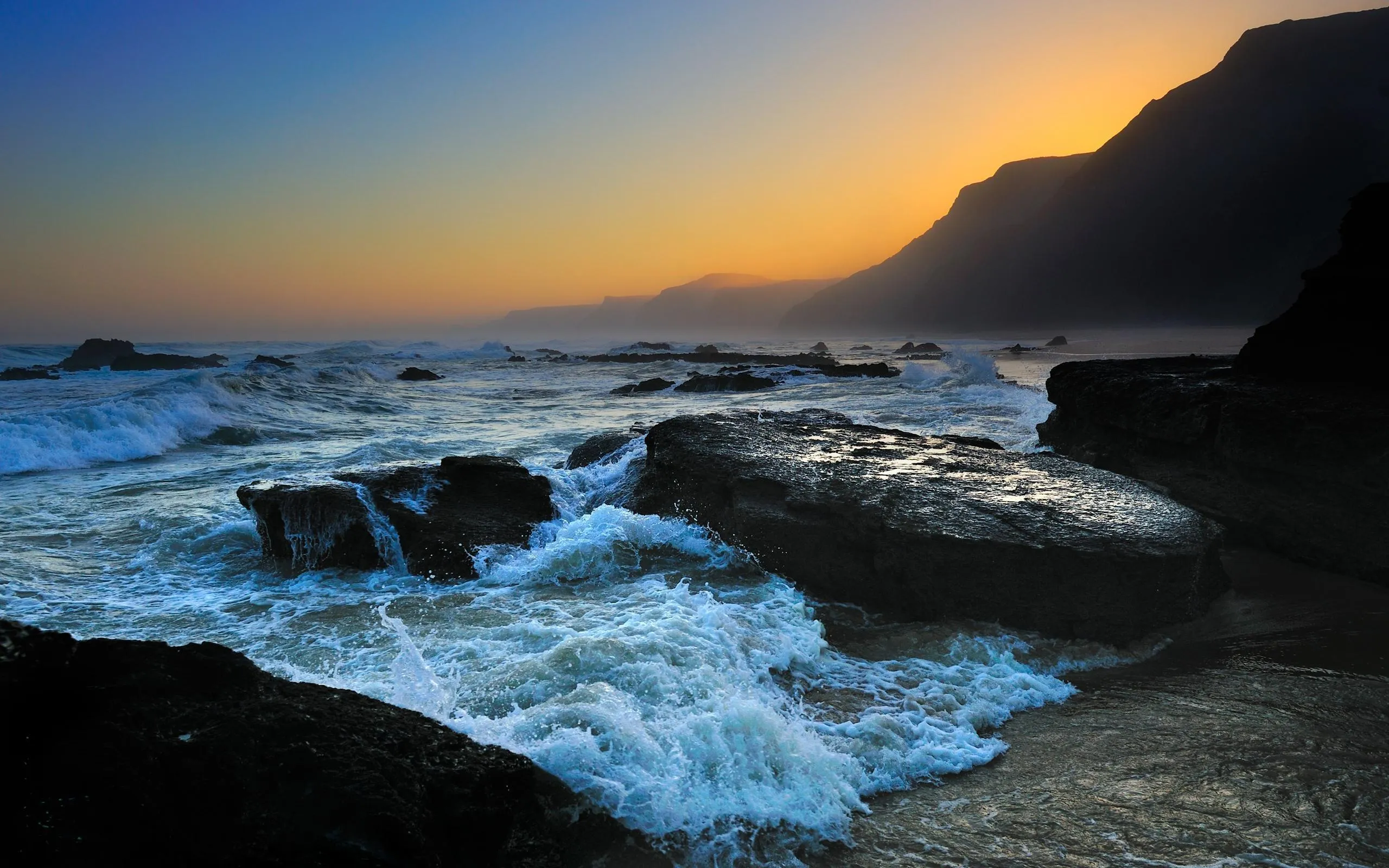 Sunlight over a Rocky Coast with Ocean Waves Free Wallpaper