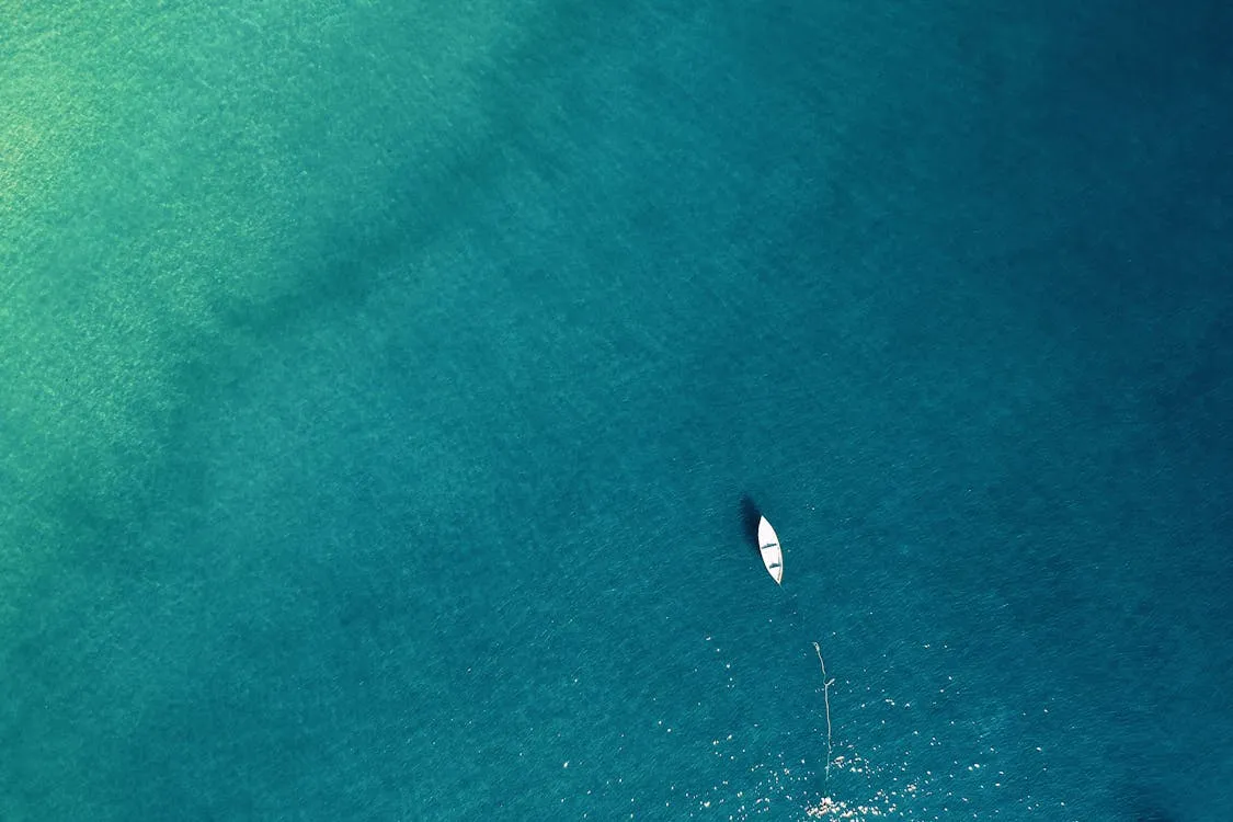 Tiny White Boat Floating in Deep Turquoise Water Wallpaper