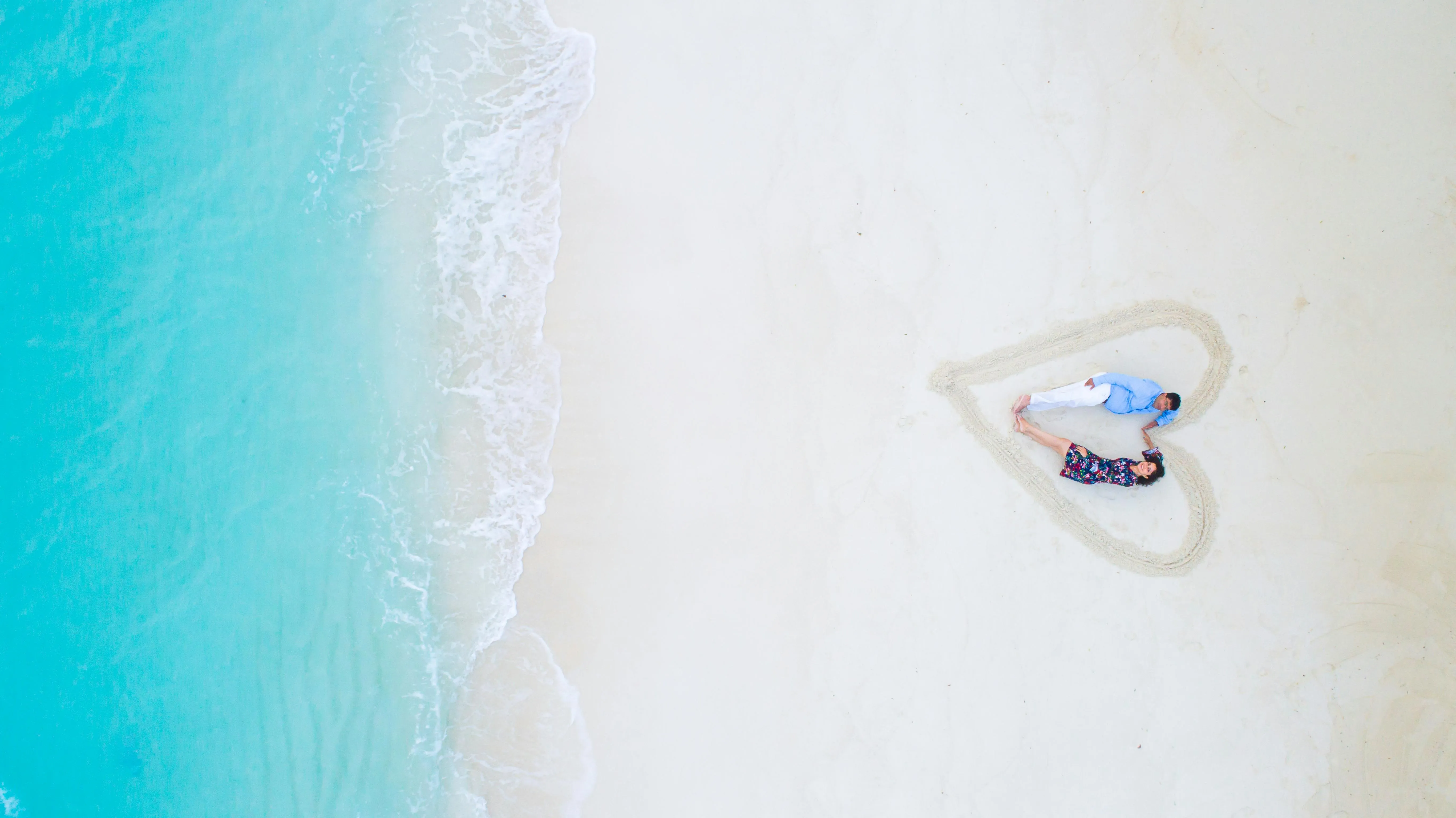 Top View of a Couple Lying on a Beach Shaped Like a Heart