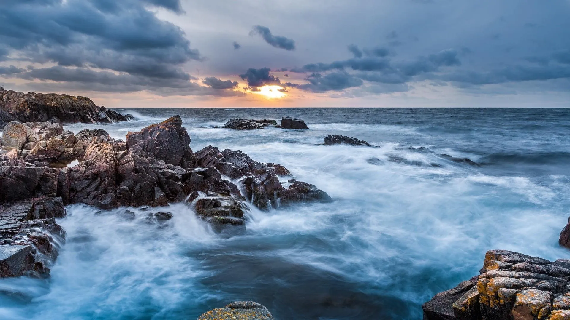Waves Crashing on Dark Rocks Beneath a Cloudy Sunset Sky