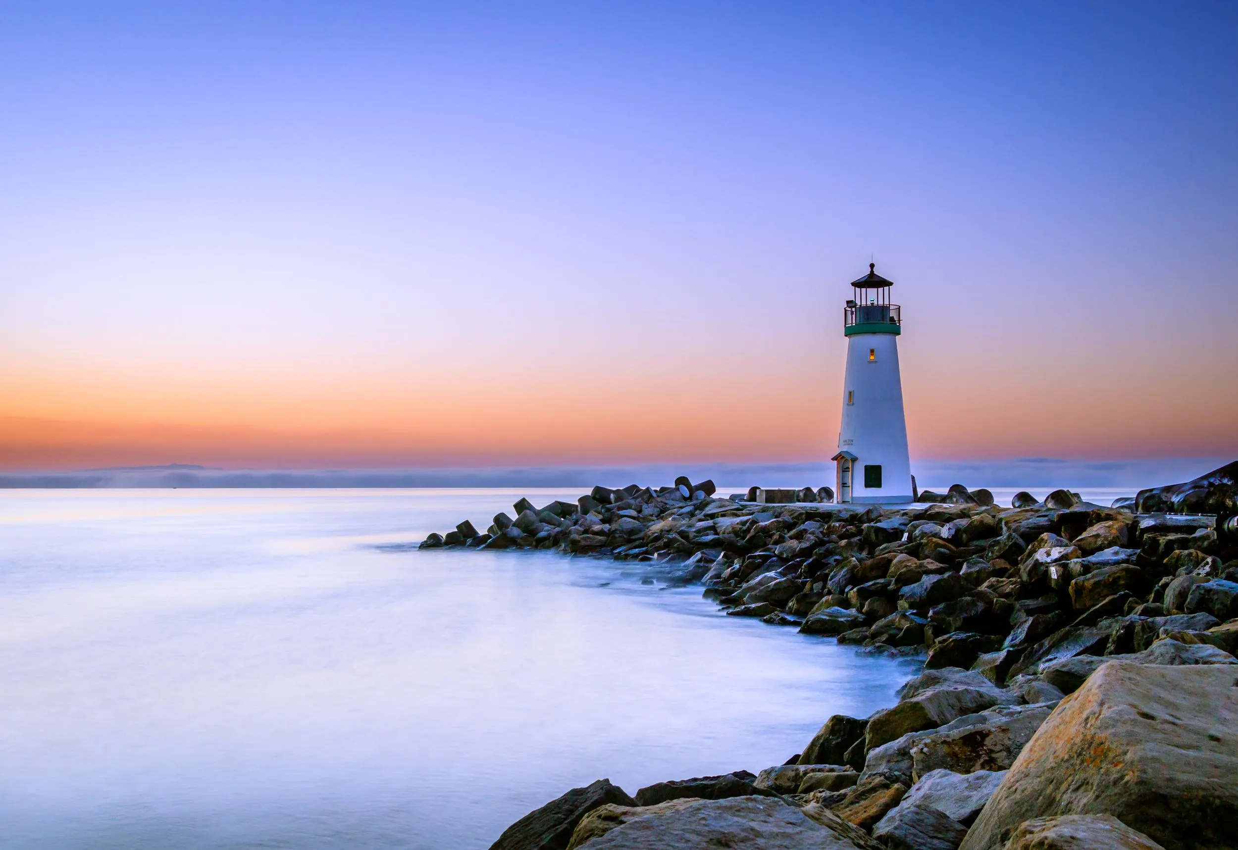 White Lighthouse on Rocky Coast with a Calm Sunset View