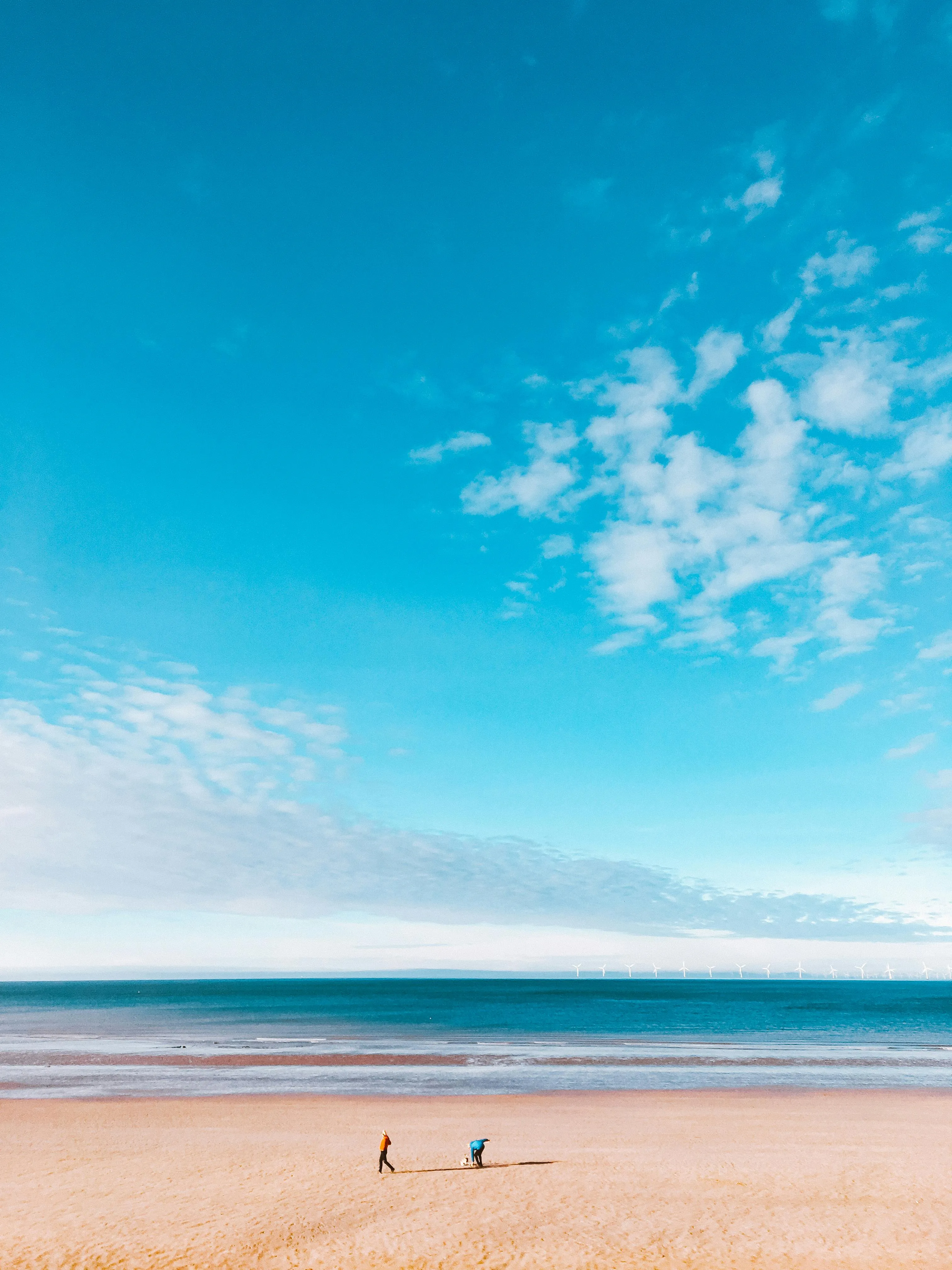 Wide Open Beach with Blue Sky and People Walking Along