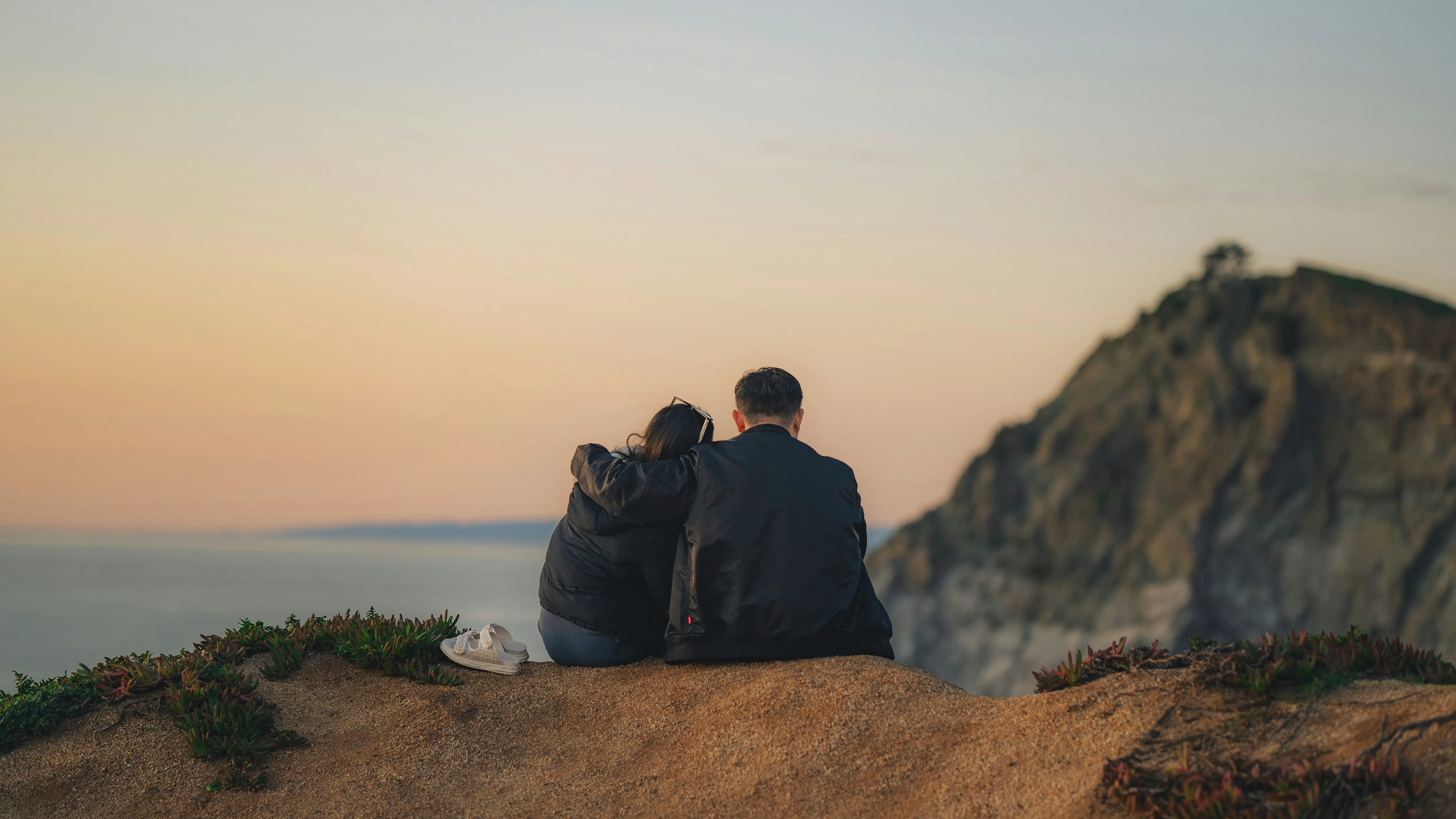 Couple Sitting on Cliff Watching Evening Sunset Wallpaper