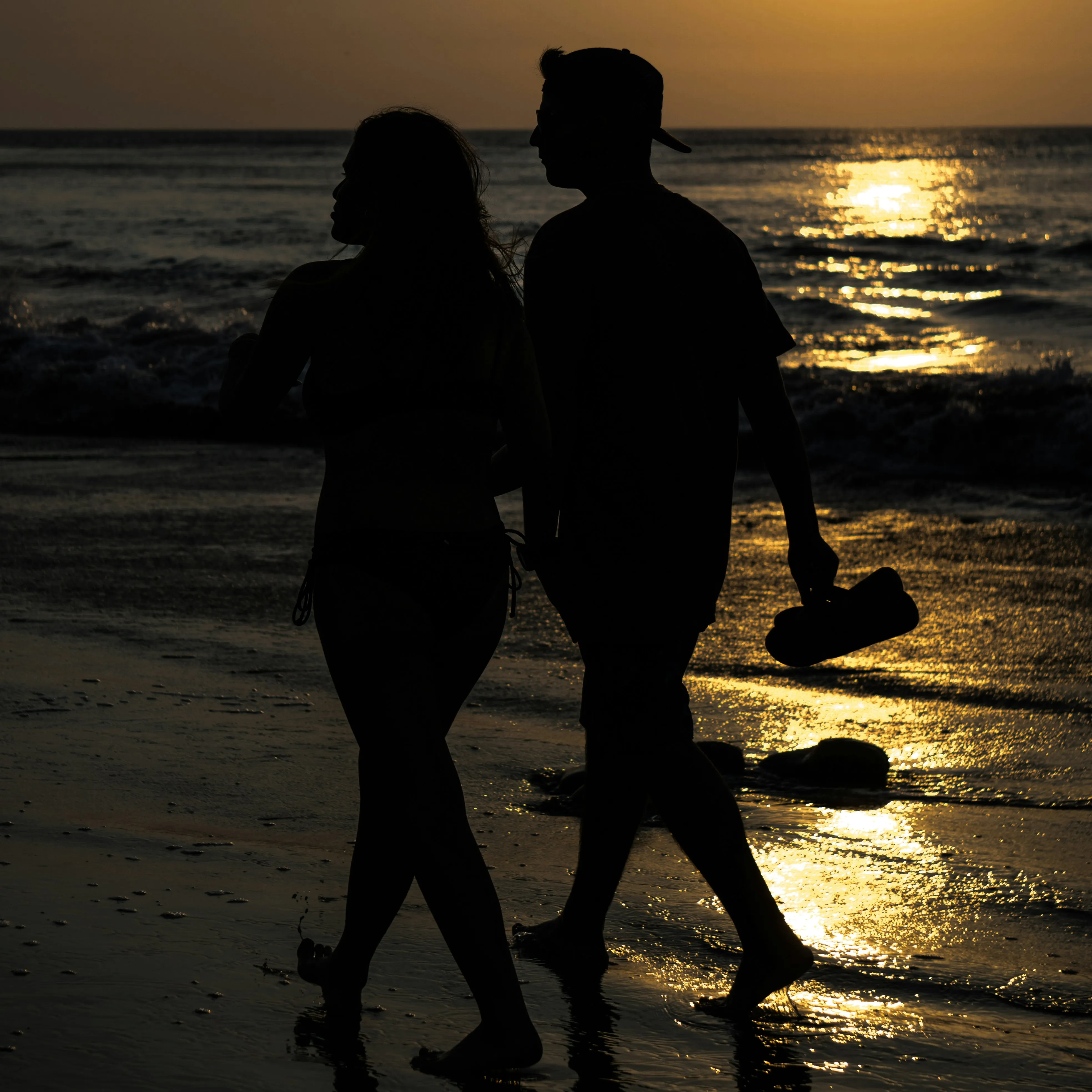 Couple Walking Silhouetted by Ocean Sunset Wallpaper