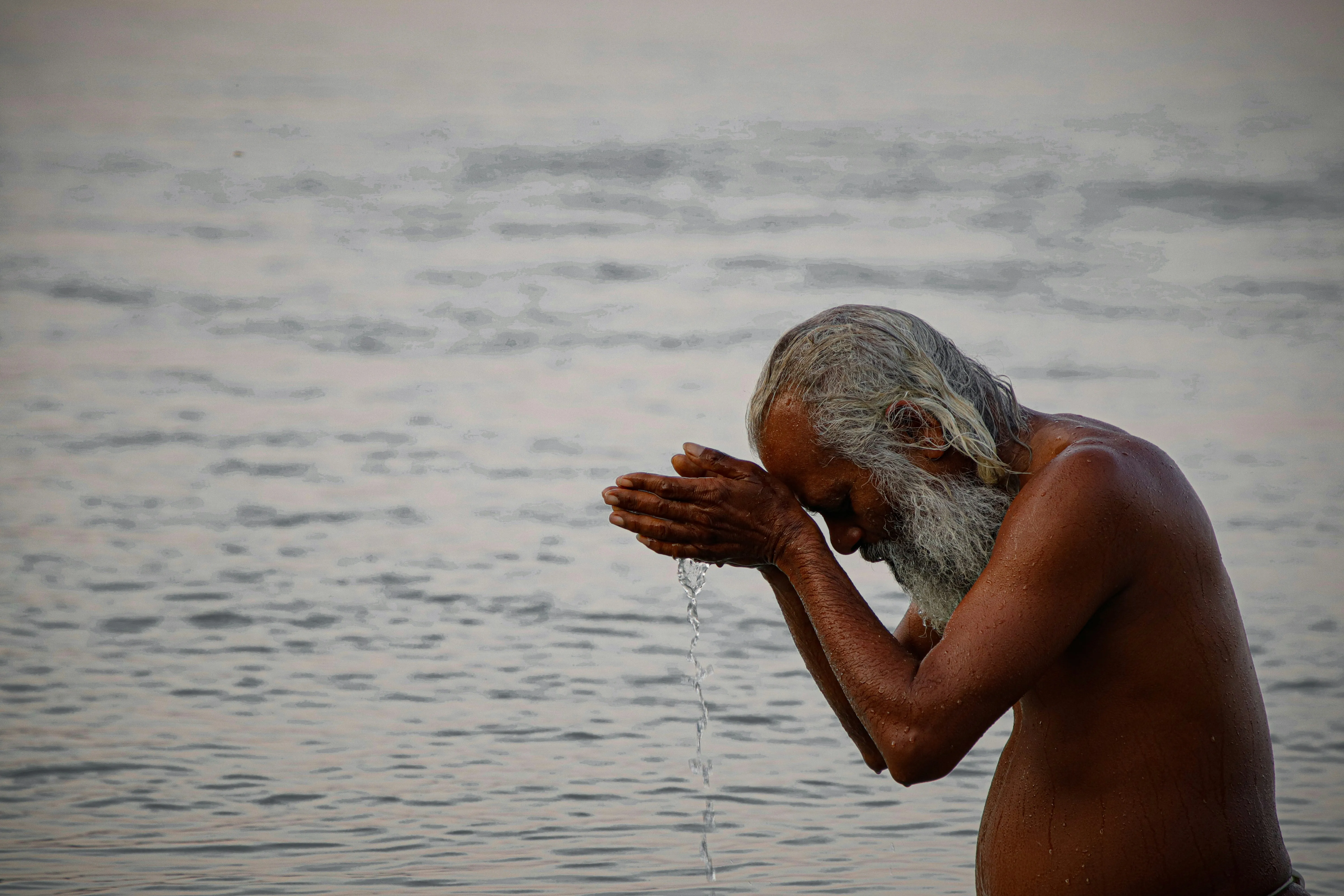 Elderly Man Praying Peacefully Beside Calm Water Wallpaper