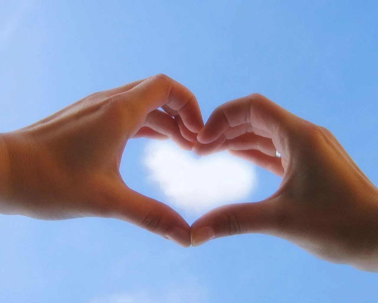 Hands Forming Heart Shape with Blue Sky Background