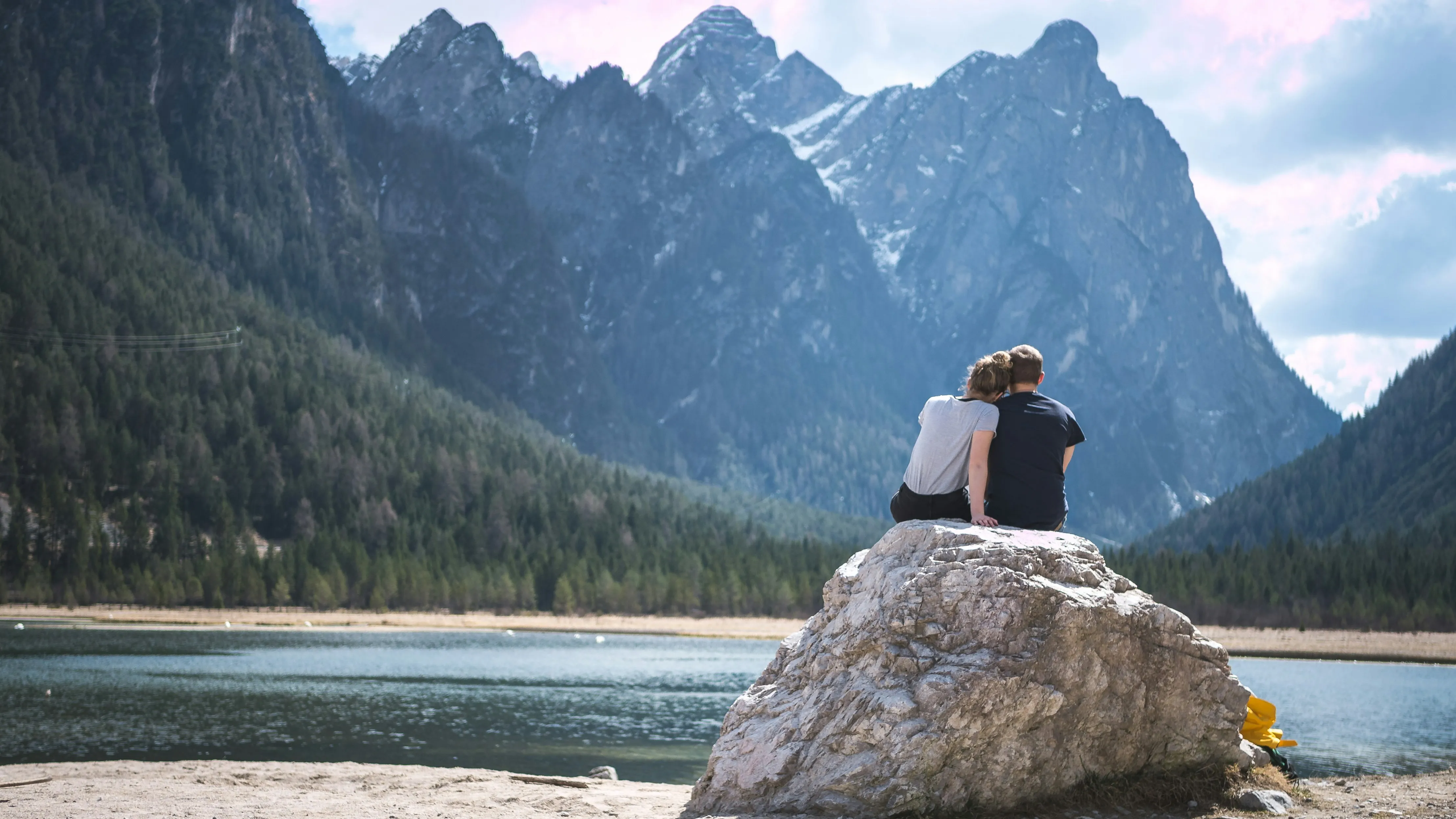 Wallpaper of Couple Sitting by Lake Surrounded by Mountains