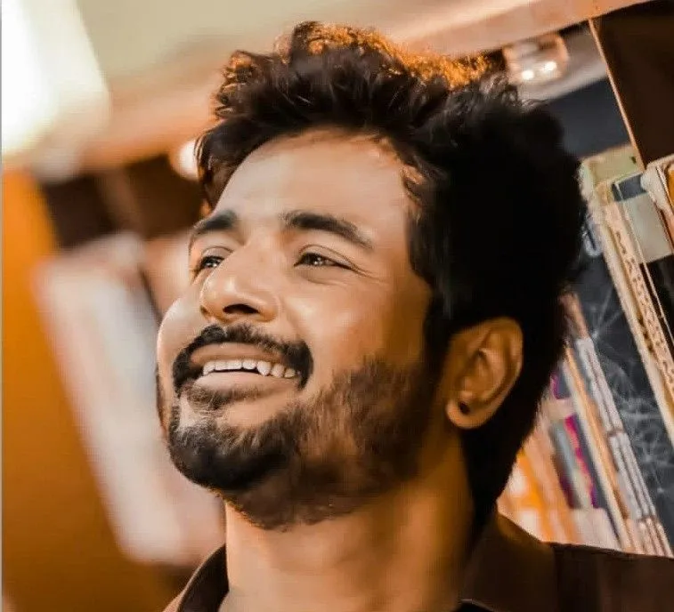 Sivakarthikeyan Laughing By Leaning on Bookshelf Wallpaper