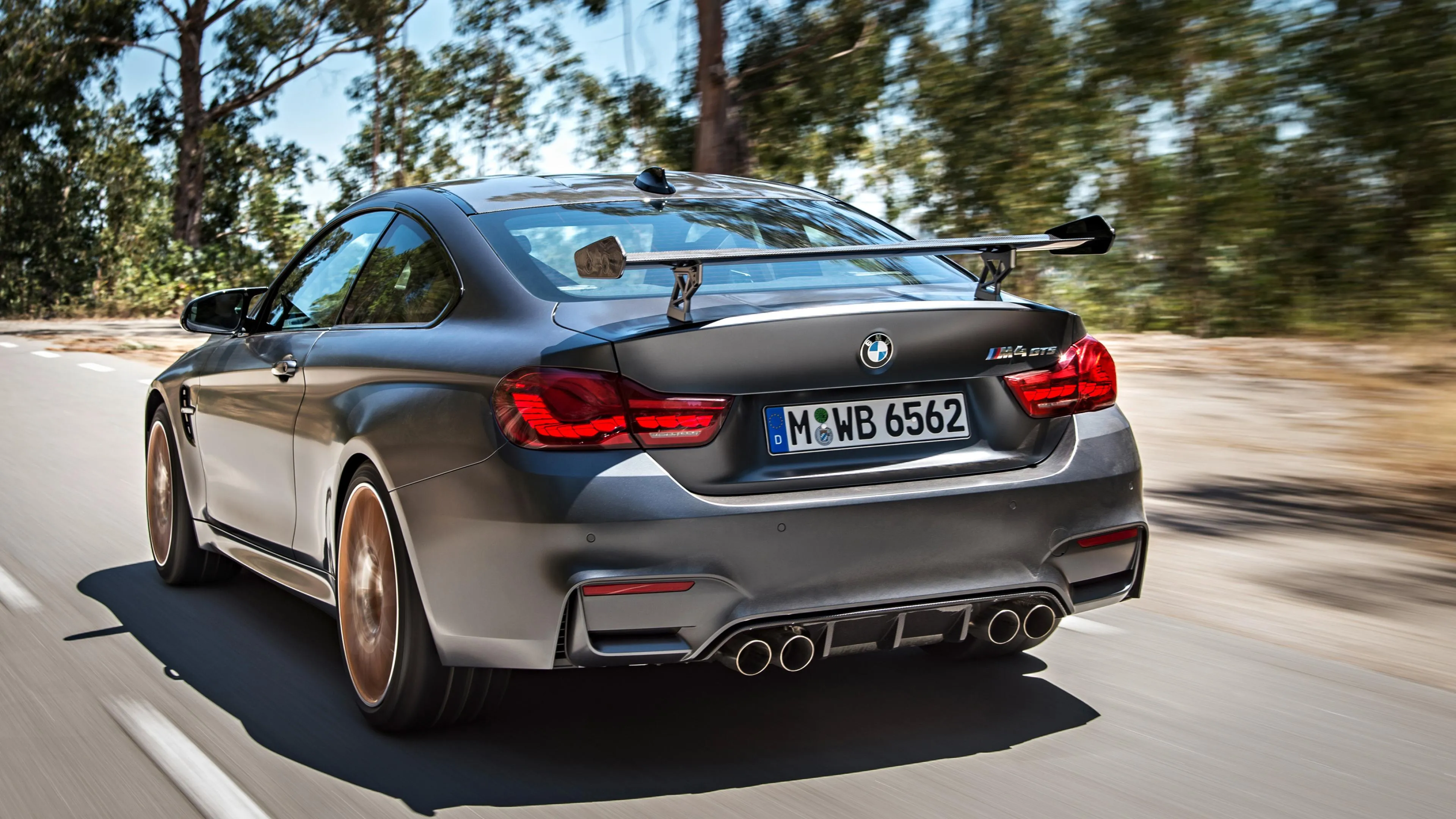 Black Bmw Driving Through Tree Lined City Street Wallpaper