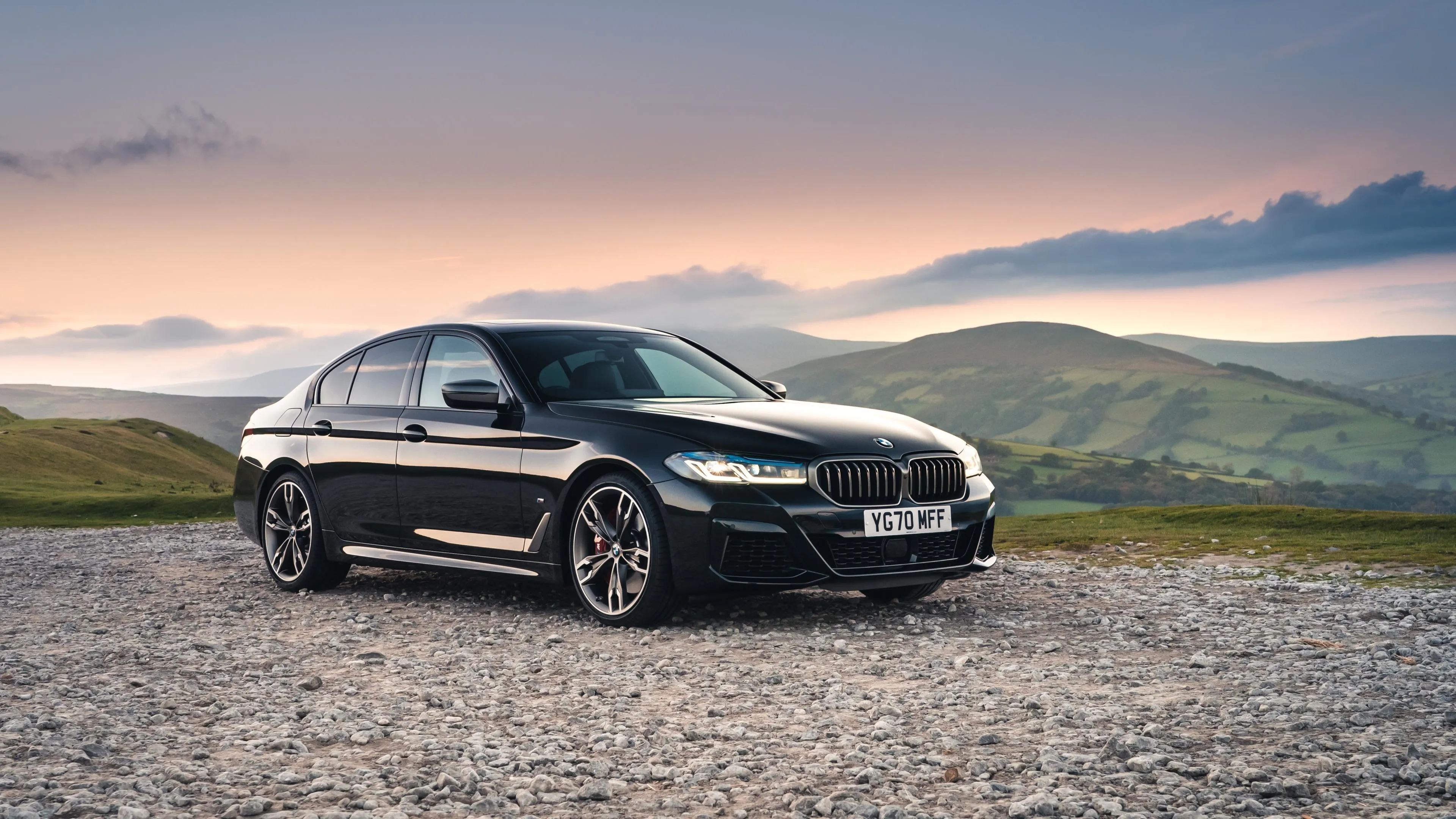 Black Bmw Sedan on Gravel Road with Hills at Dusk Wallpaper