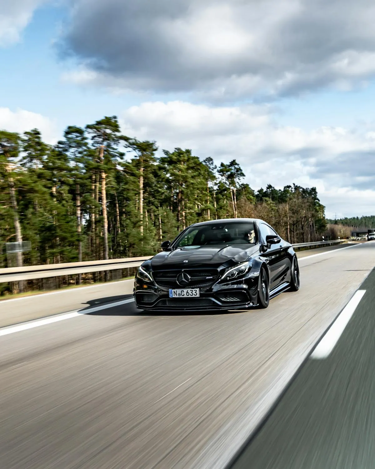 Black Mercedes on Open Highway Surrounded by Forest