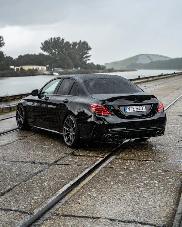 Black Mercedes sedan parked on wet road near water image