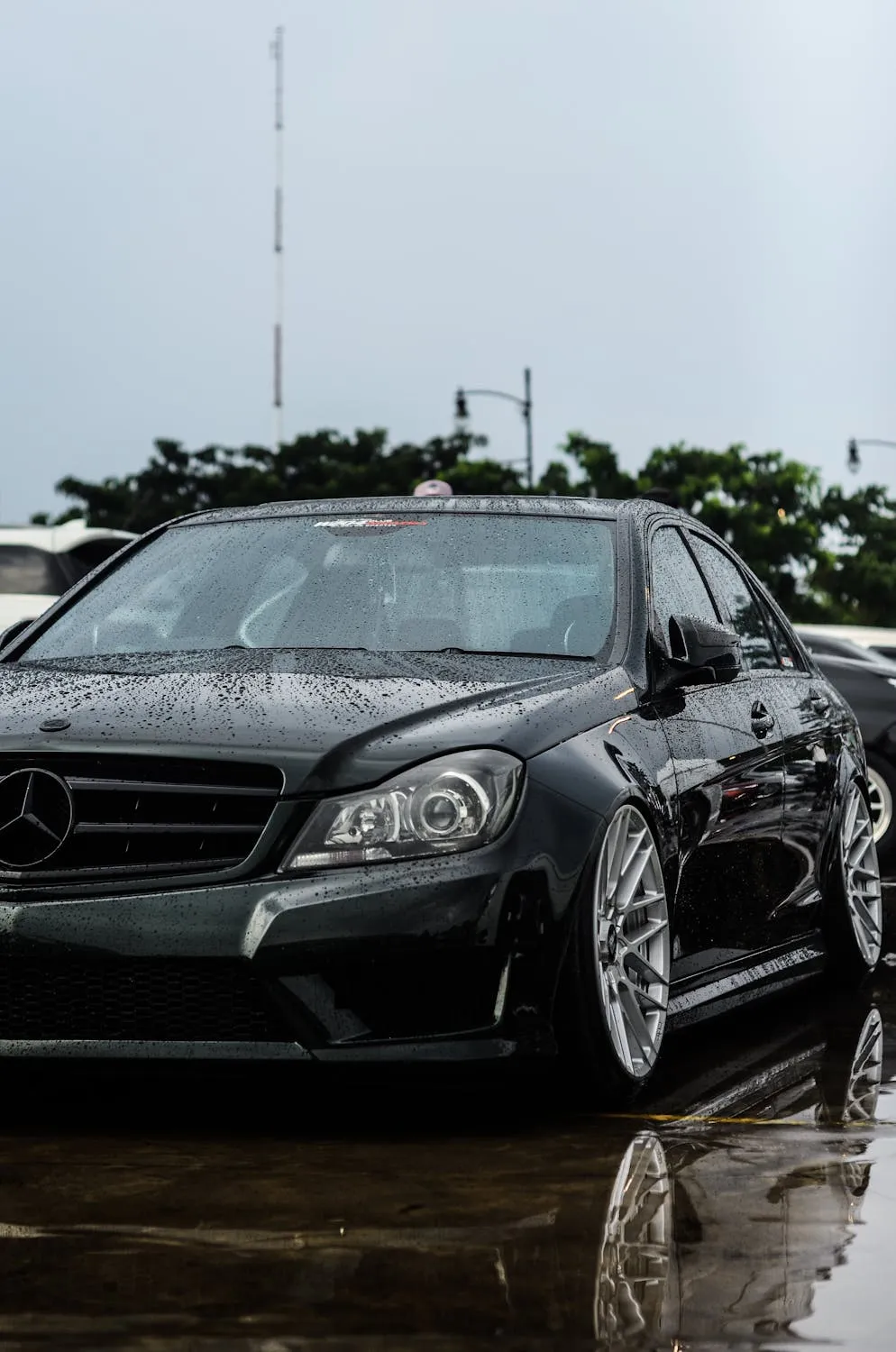 Black Mercedes Sedan Parked on Wet Road Reflecting Sky