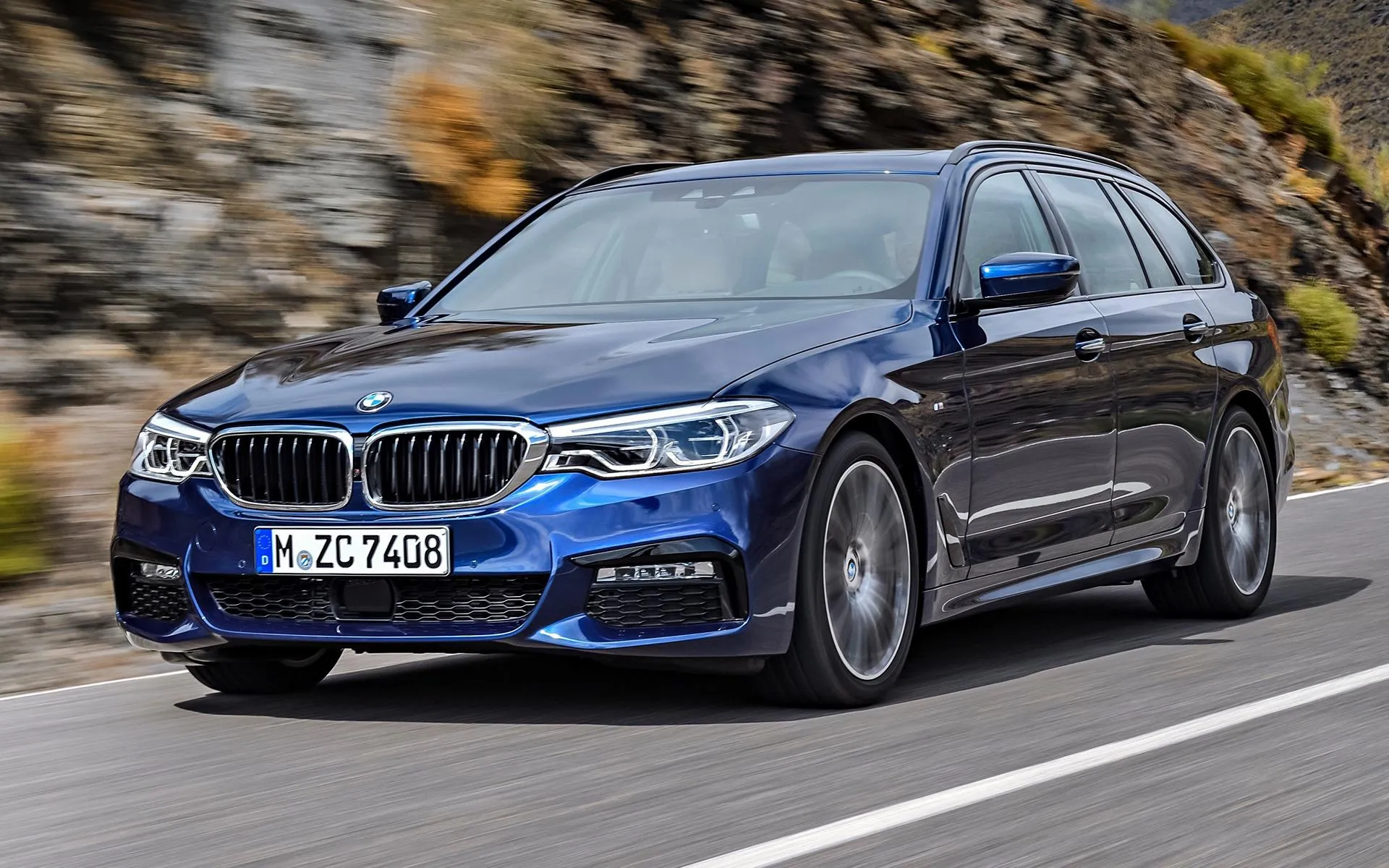 Blue Bmw Cruising Down a Tree Lined Suburban Road Wallpaper