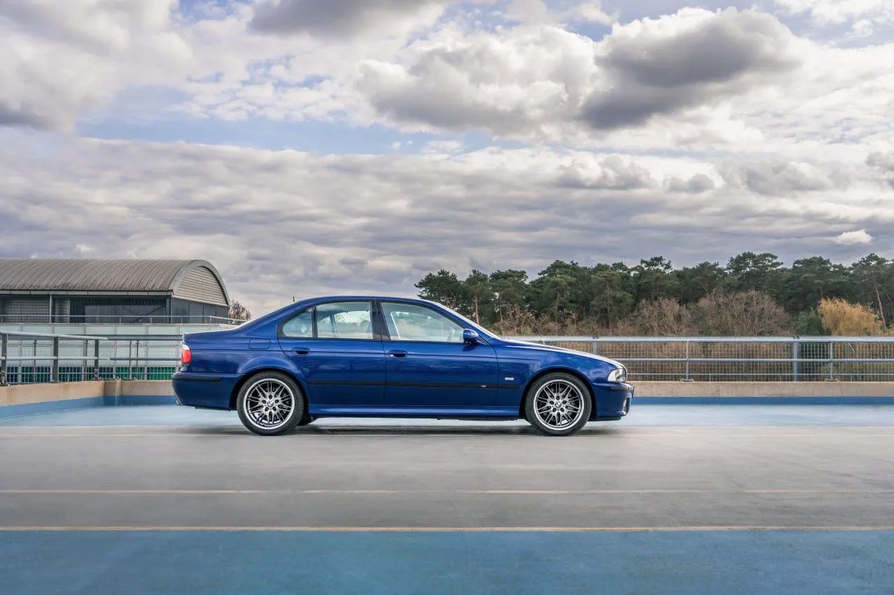 Blue Bmw Sedan Speeding Along Track with Dramatic Clouds