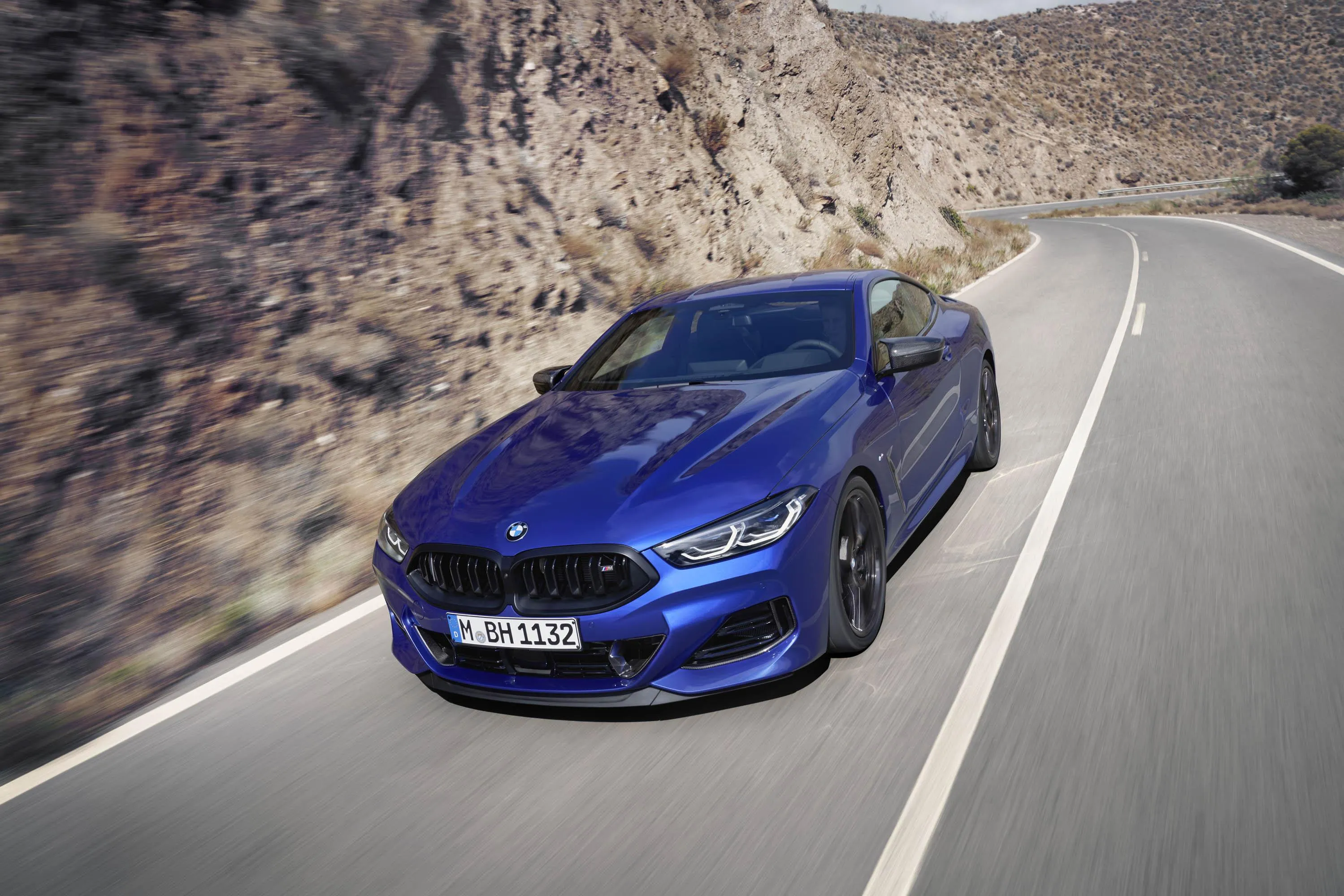Blue Bmw Speeding Along Scenic Cliffside Road Wallpaper