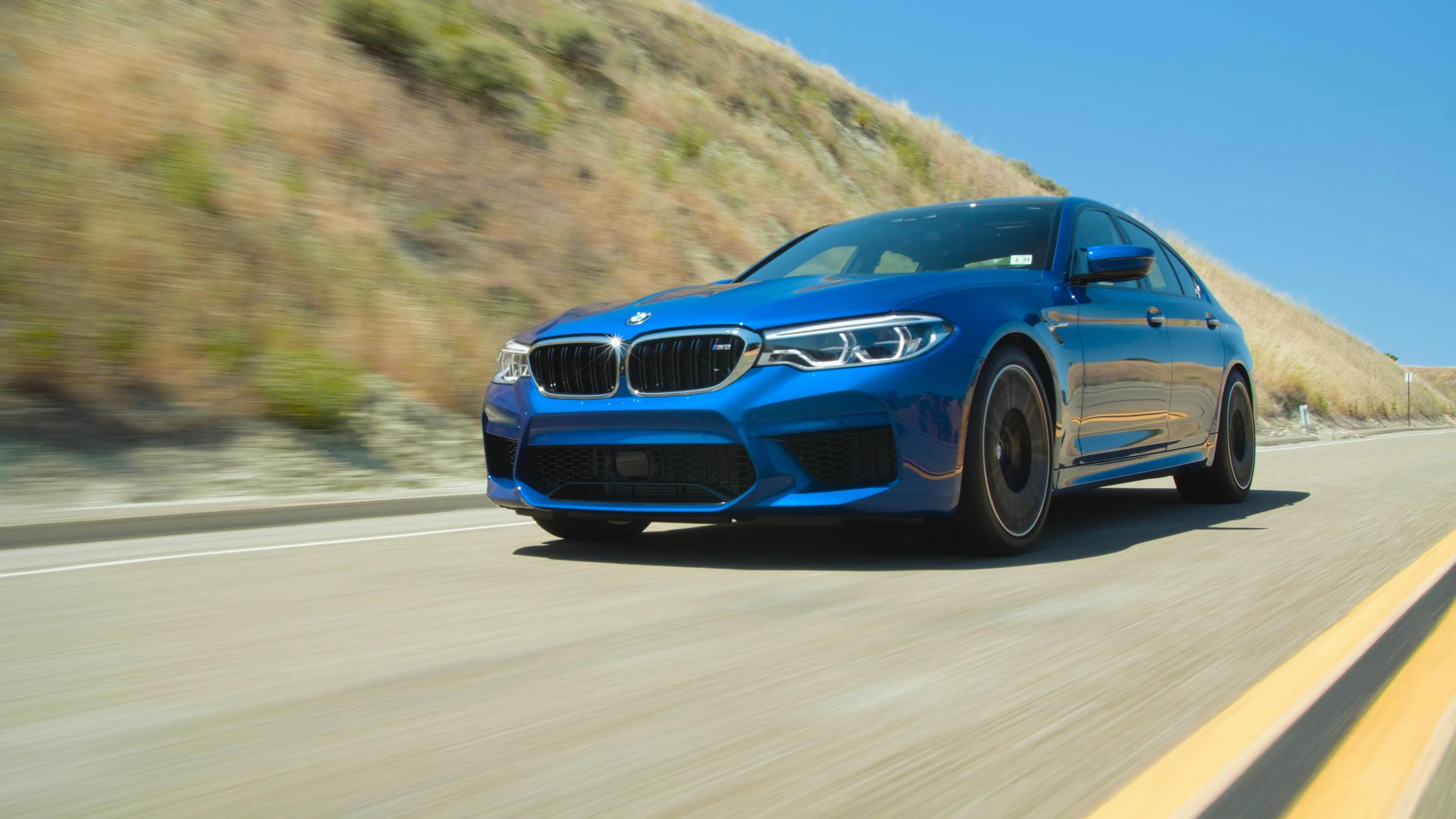 Blue Bmw Speeding Down Desert Highway in Sunshine Wallpaper