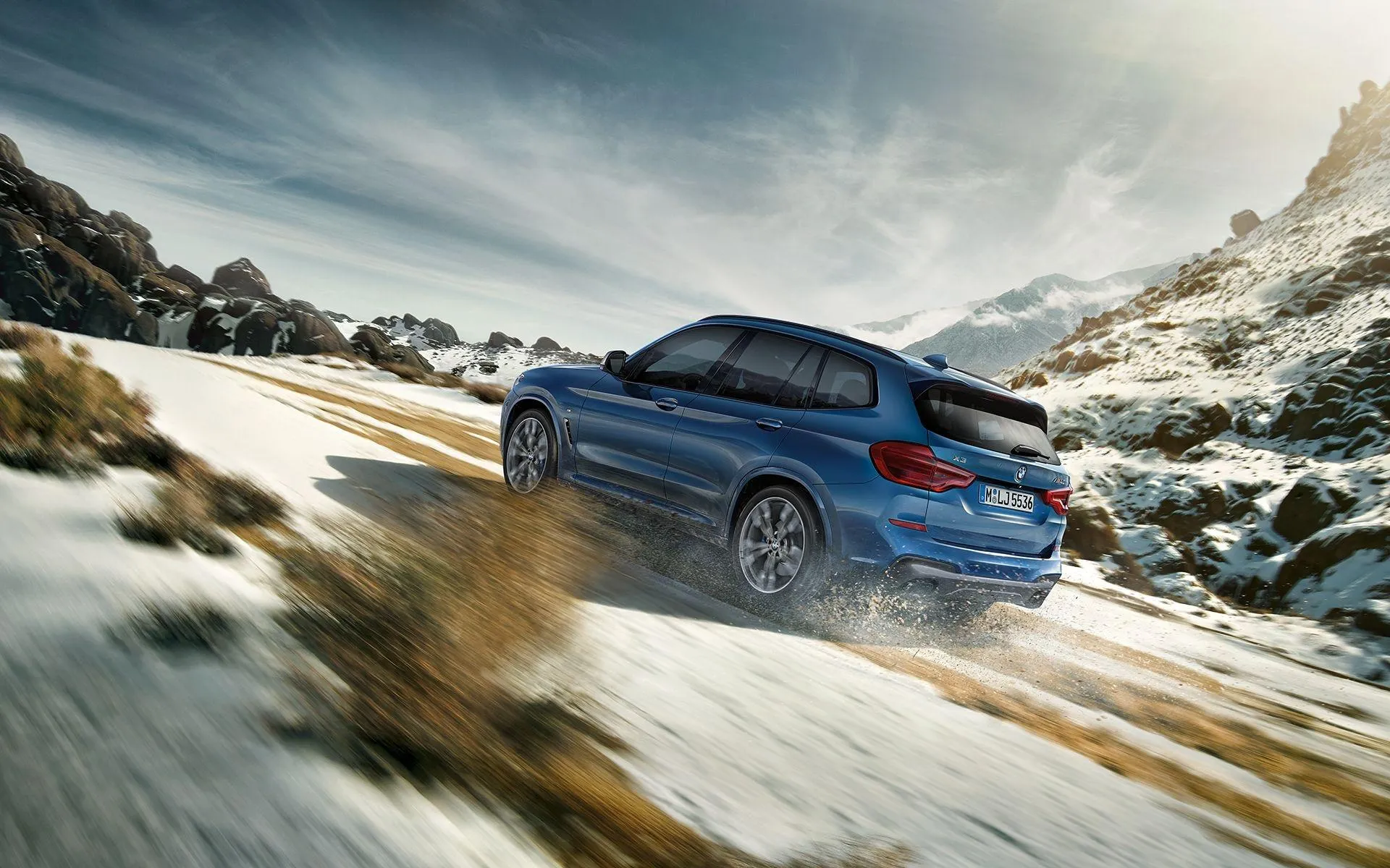 Blue Bmw Suv Driving Through Snowy Mountain Terrain