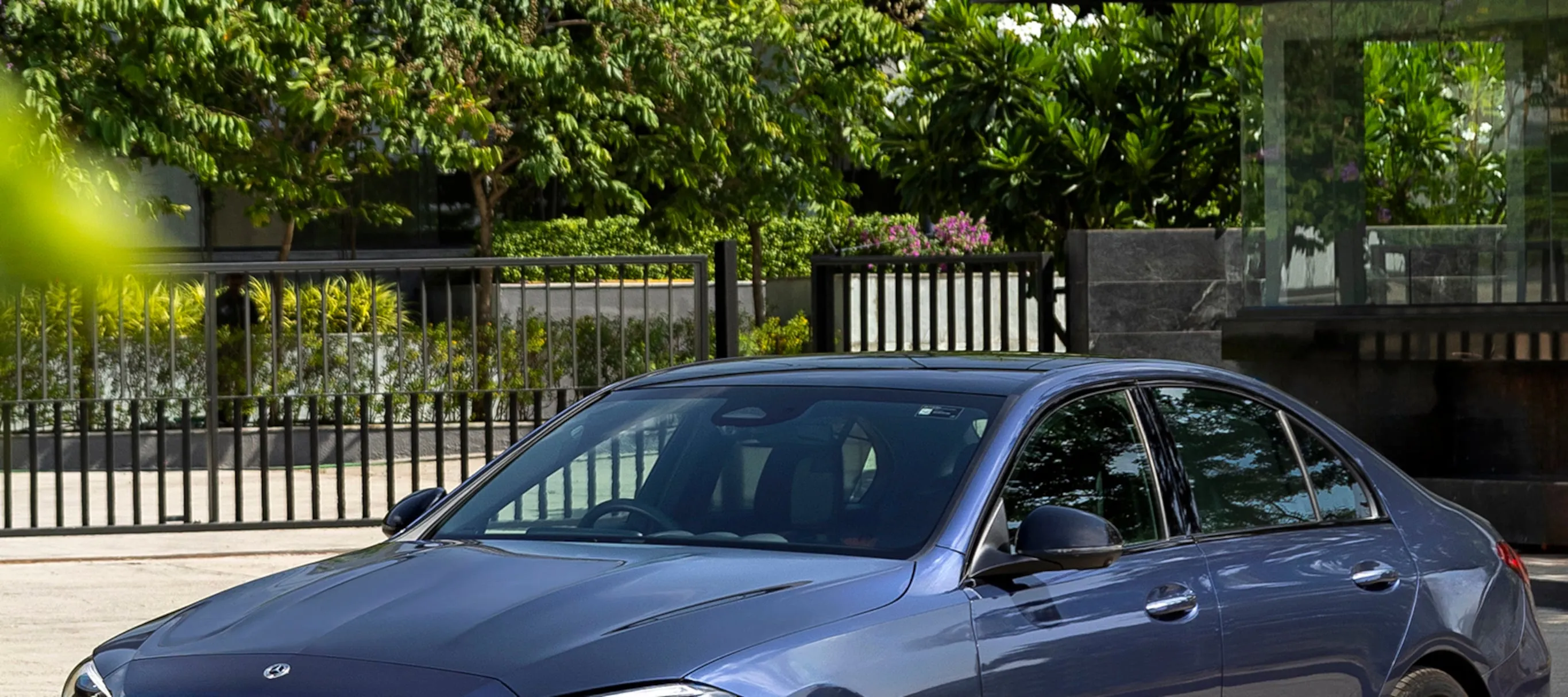 Blue Mercedes Benz parked near a fence in a green environment
