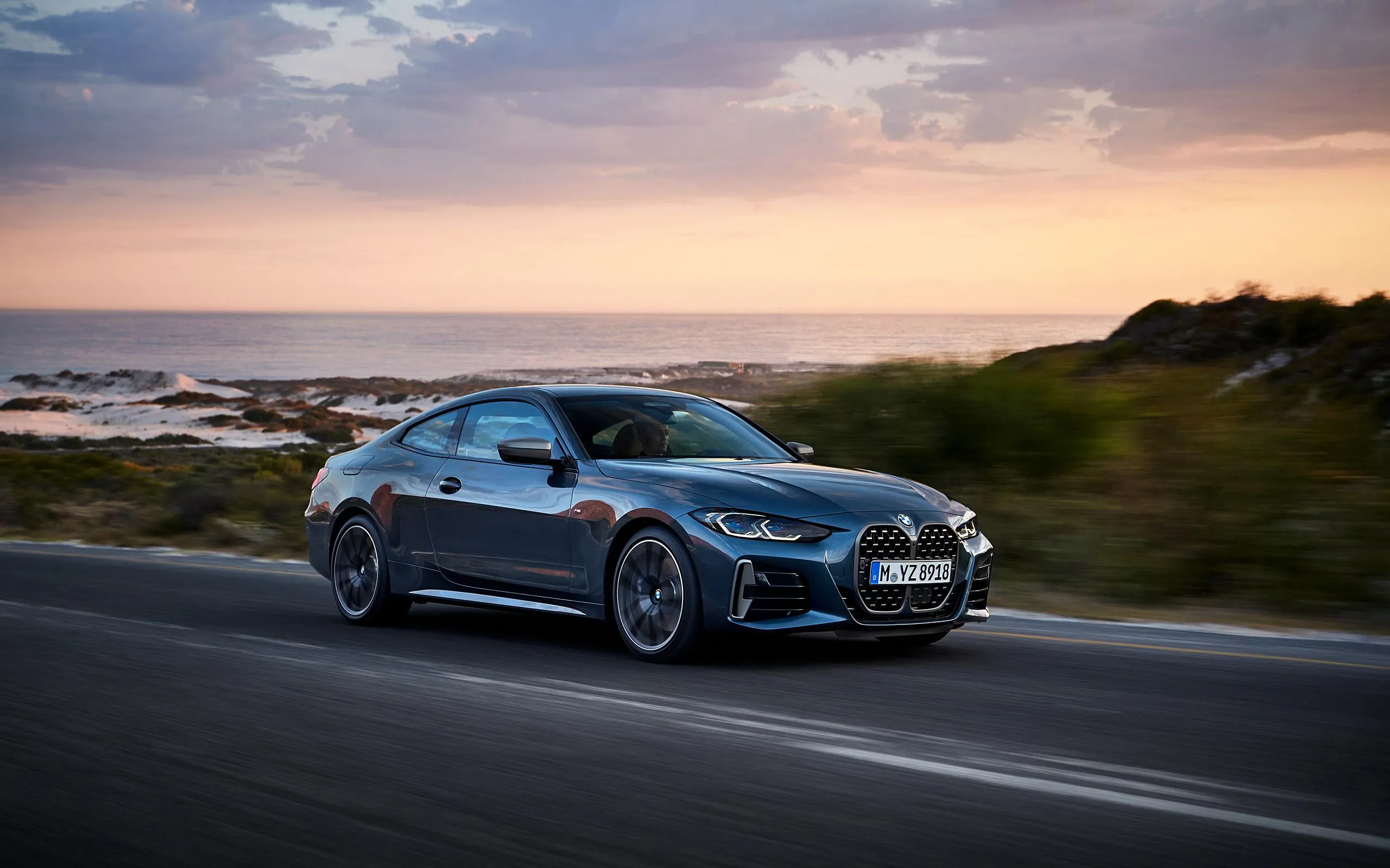 Bmw Blue Coupe Driving Fast Along Road at Sunset Wallpaper
