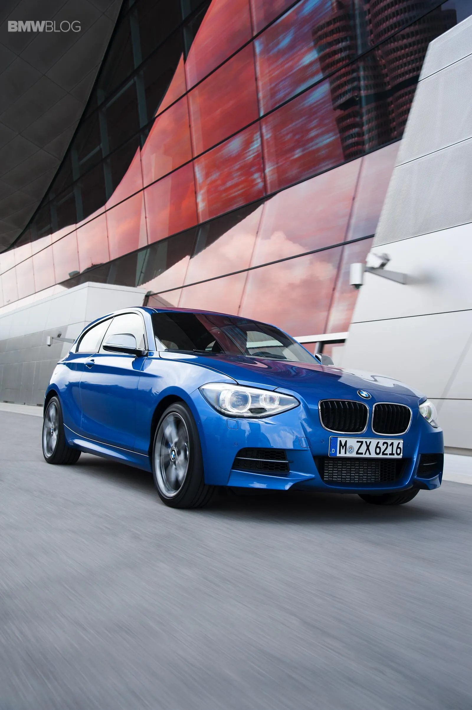 Bmw Blue Sedan Driving Fast By Modern Building Wallpaper