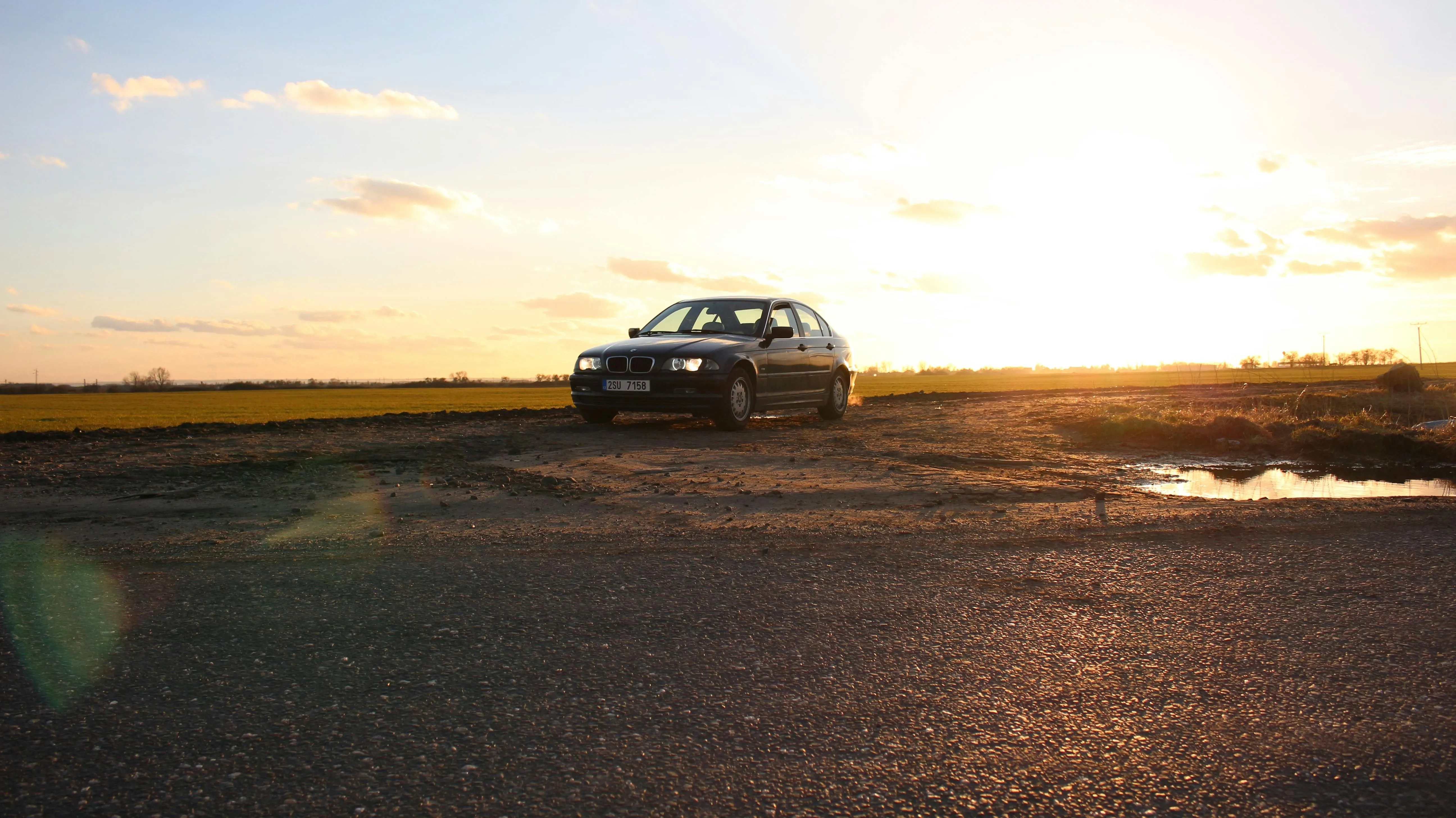 Bmw Driving at Sunset on a Wet Road Reflecting Golden Light