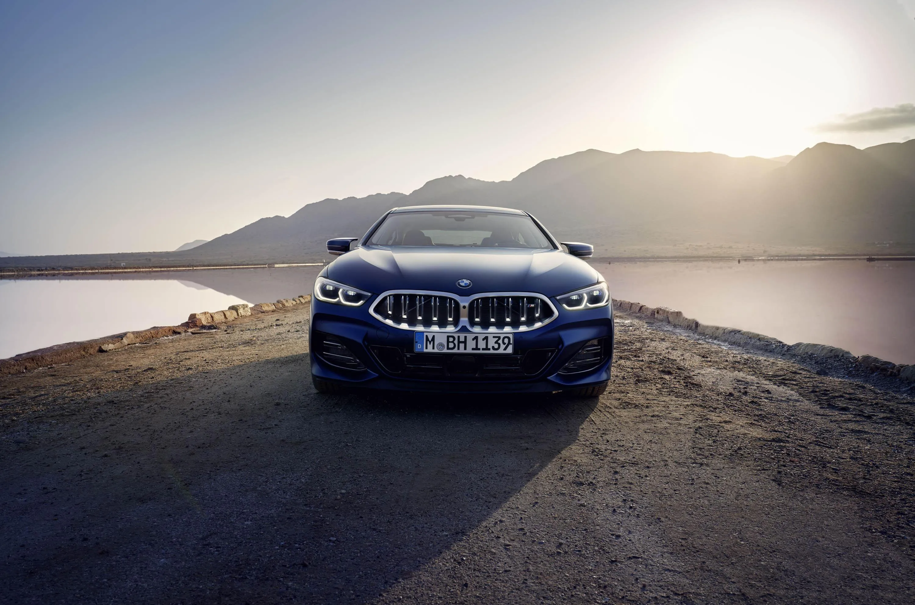 Bmw Parked on Coast with Sun Setting Behind Mountain