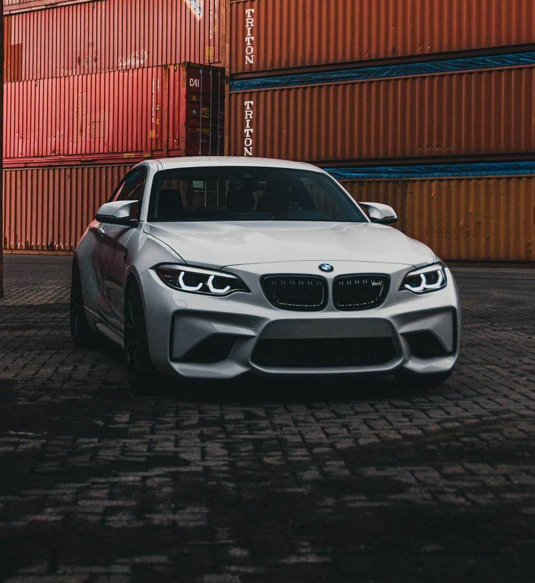 Bmw Sport Sedan Parked Next To Containers at Dusk Wallpaper