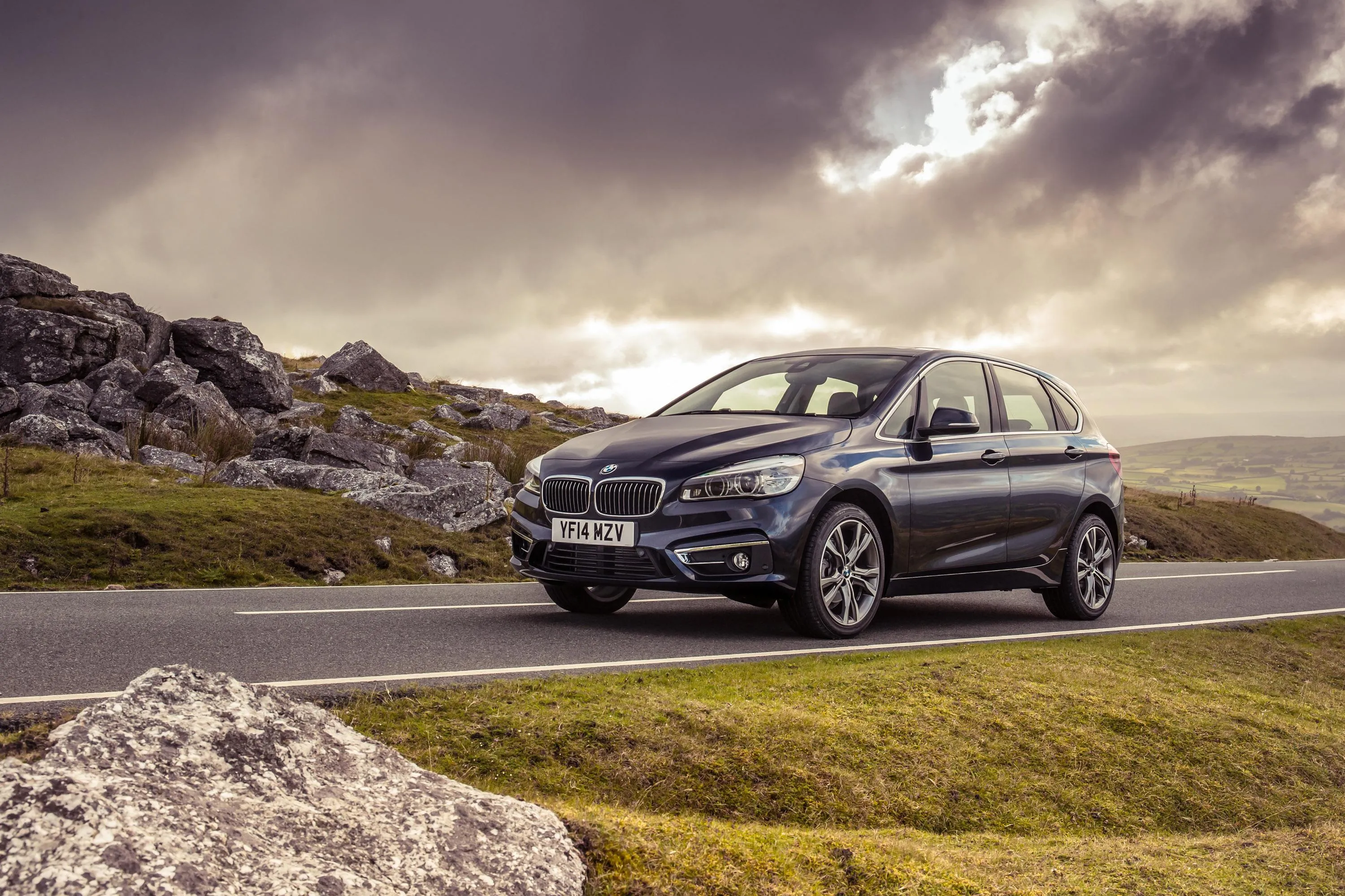 Bmw Suv Parked Near Rocky Hill with Dramatic Cloudy Sunset