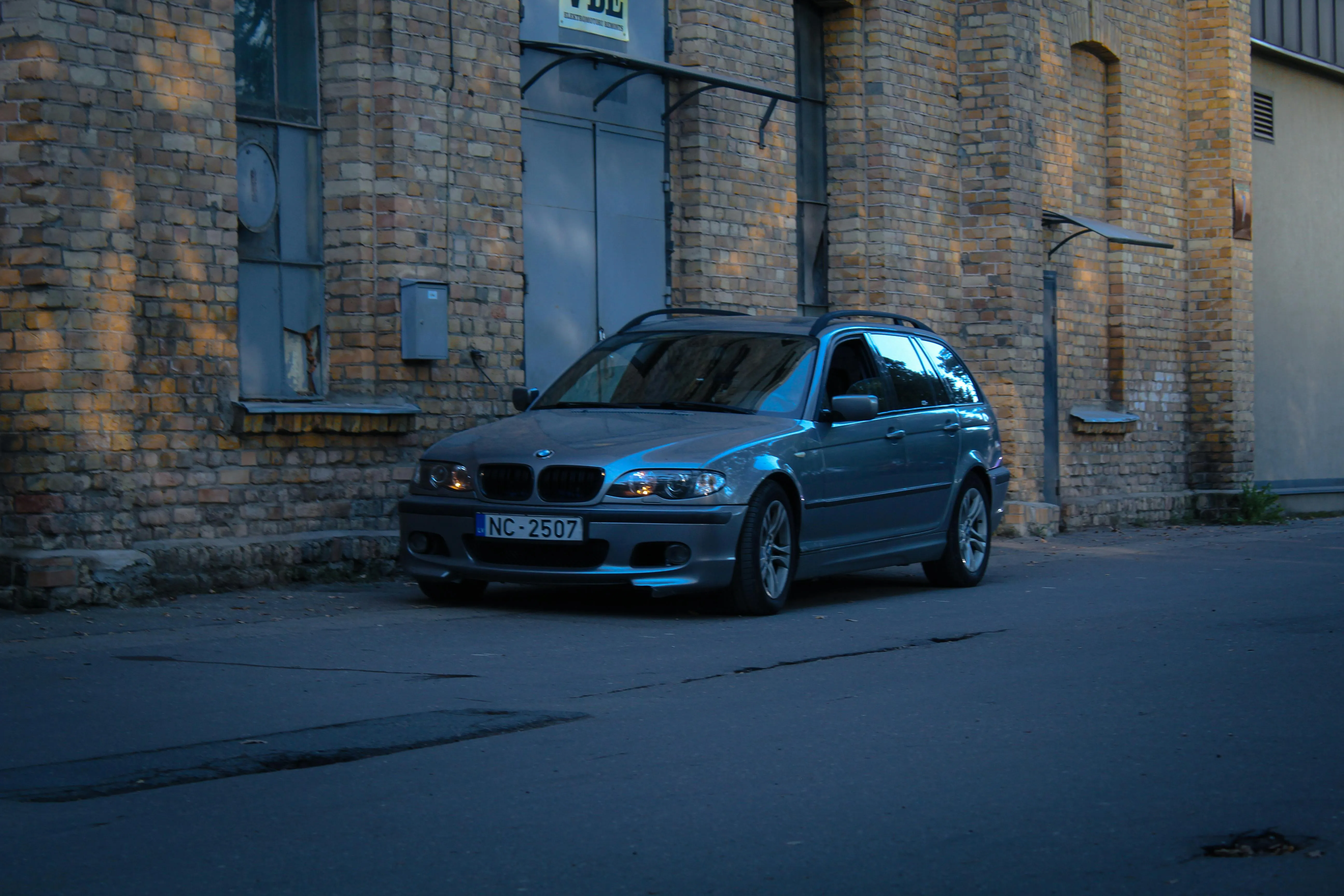 Dark Bmw Parked on Quiet Street Beside Brick Wall Image